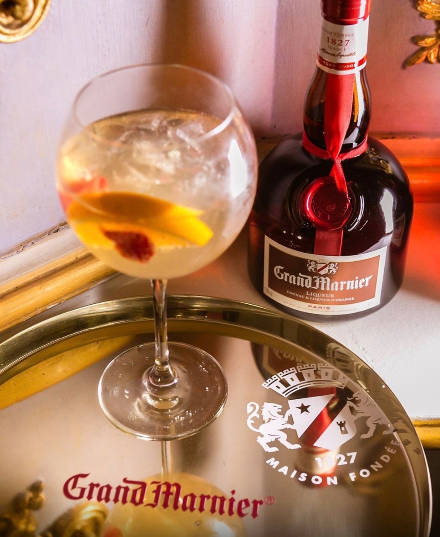 Glass of Grand Marnier cocktail with orange slices beside a bottle on a decorative tray.