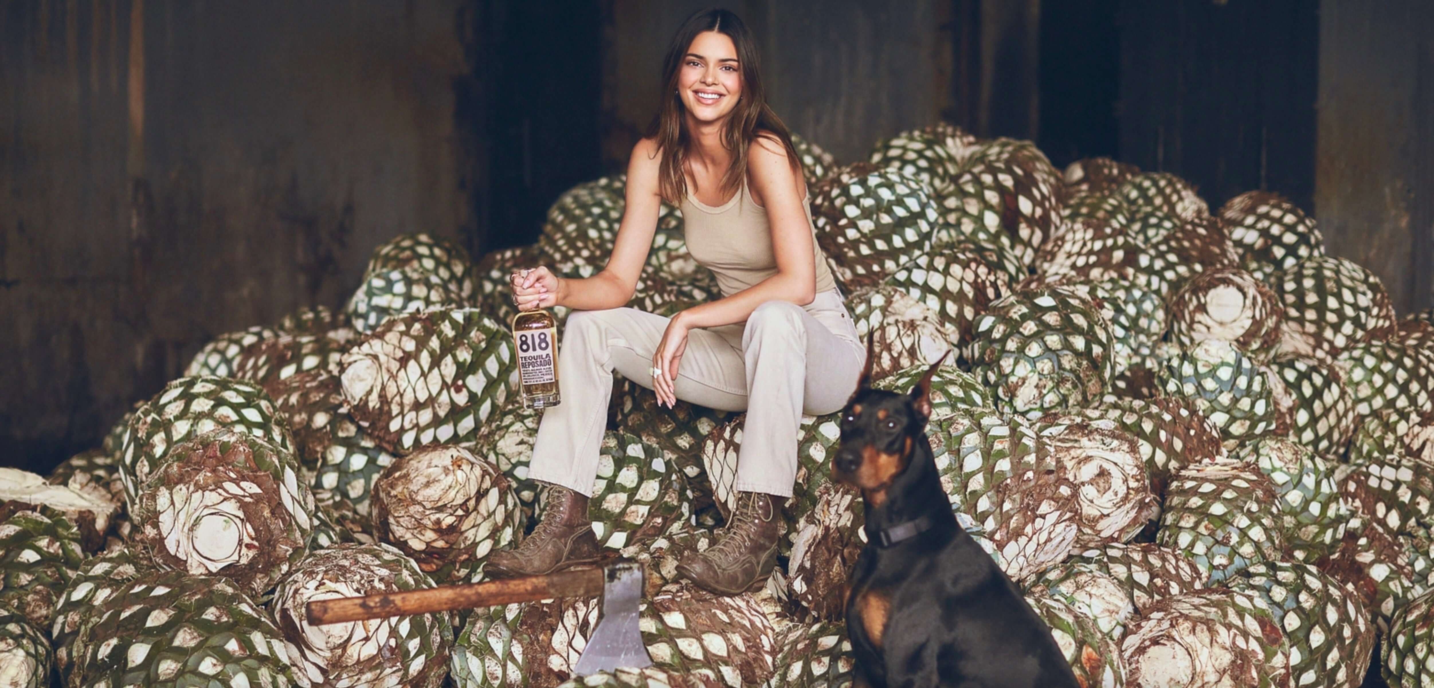 Kendall Jenner holding 818 Reposado Tequila on a pile of agave with a dog, showcasing the tequila's authentic roots.
