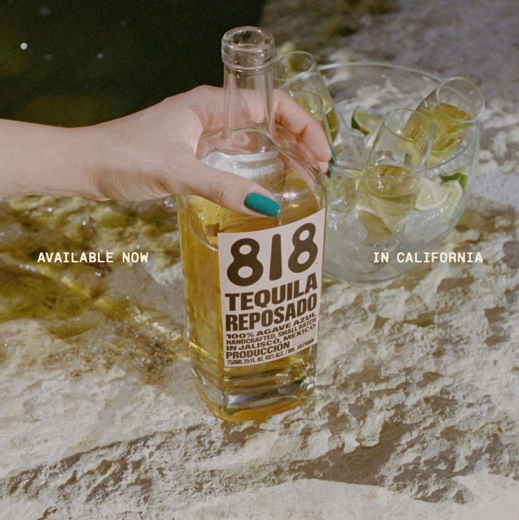 Hand holding 818 Reposado Tequila bottle with cocktails nearby, promoting availability in California.