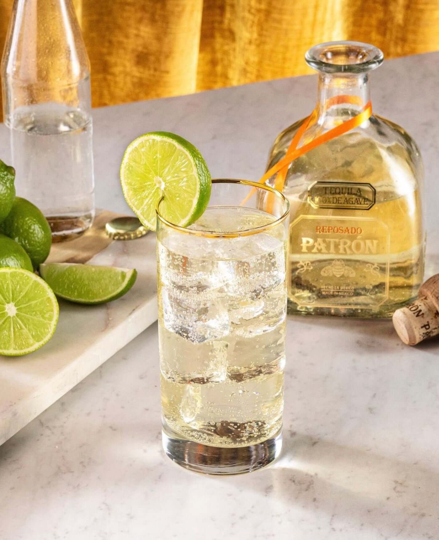 Patrón Reposado tequila cocktail served with fresh lime slices and sparkling water on a marble countertop.