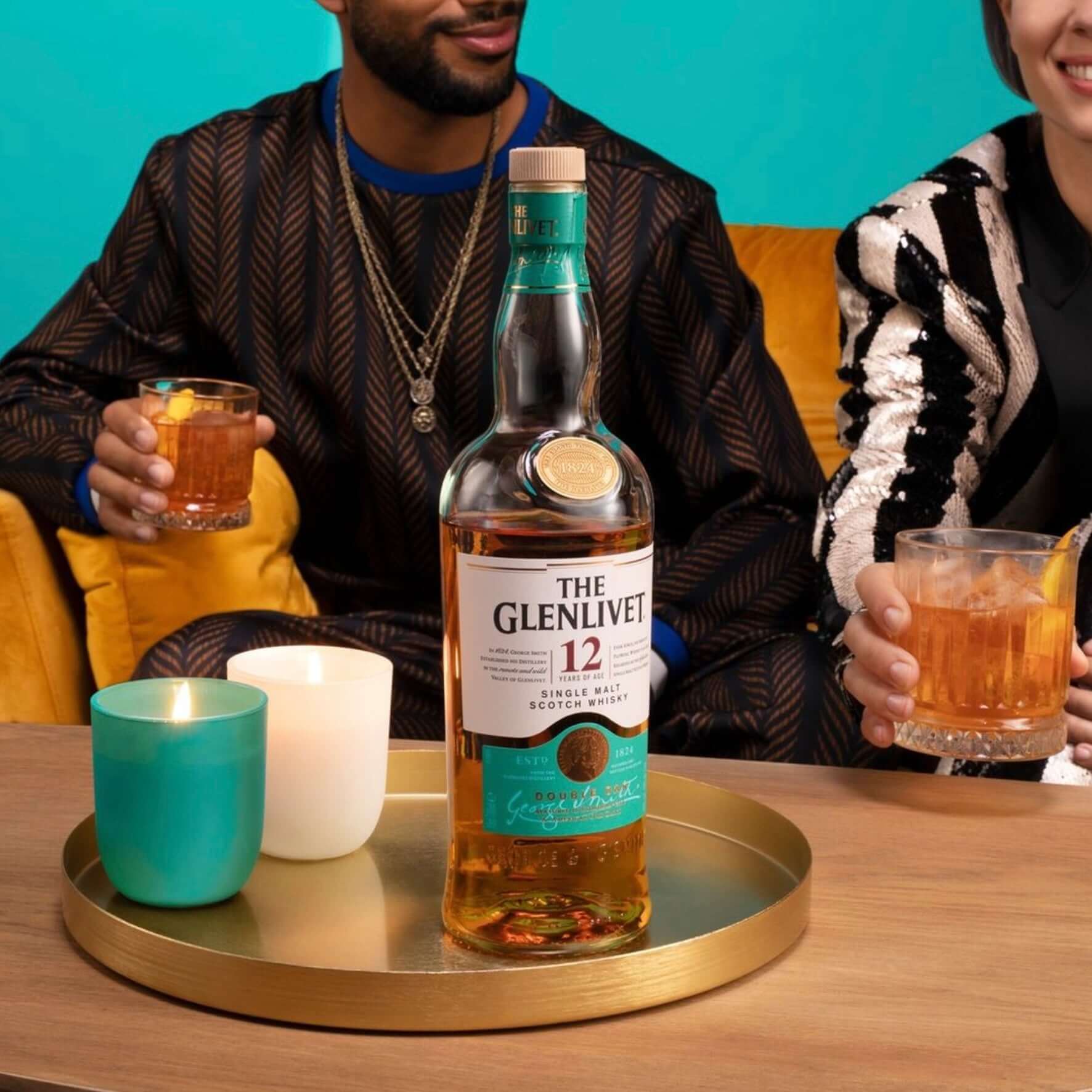 The Glenlivet 12 Year whisky bottle with drinks and candles on a stylish tray, perfect for indulgent moments.