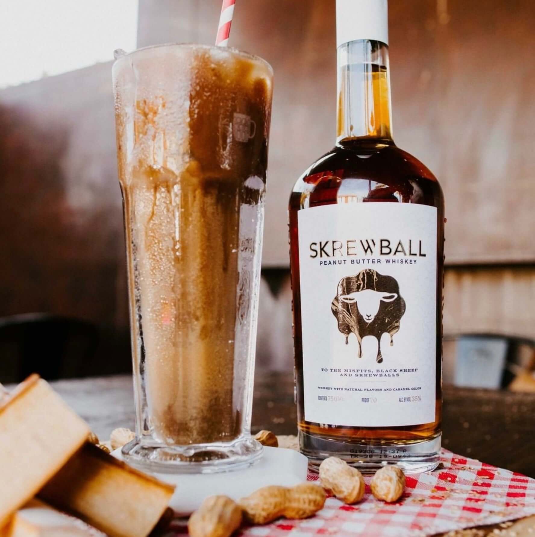 Skrewball Peanut Butter Whiskey bottle alongside a peanut butter whiskey cocktail and snacks on a table.