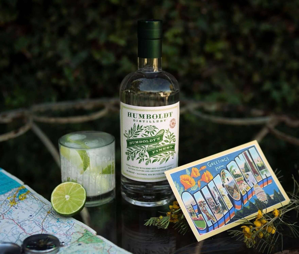 Humboldt's Finest Hemp-Infused Vodka bottle with a refreshing drink, lime, and a postcard on a table.