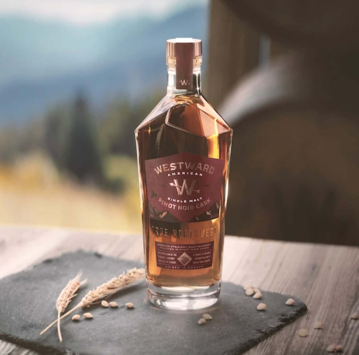 Elegant Westward American Single Malt Pinot Noir Cask Whiskey bottle on a rustic slate surface, showcasing its vibrant hue.