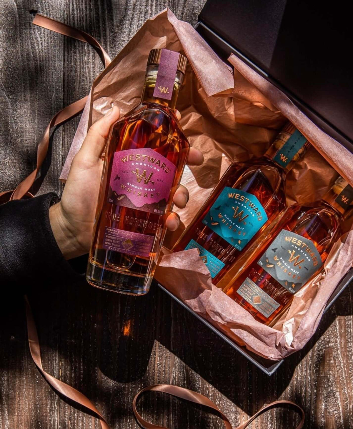 Hand holding a gift box containing Westward American Single Malt Pinot Noir Cask Whiskey and other spirits.