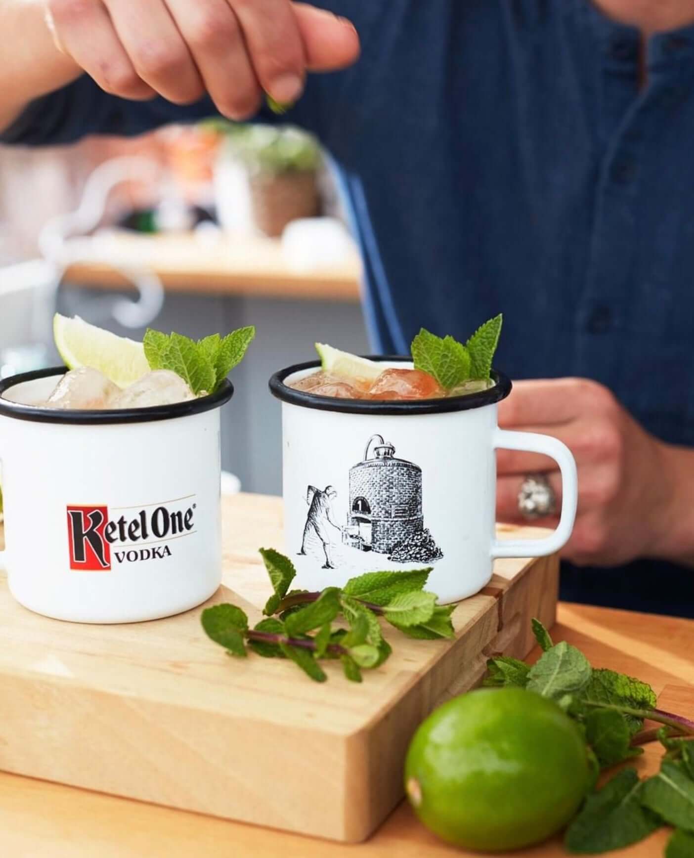 Person preparing cocktails with Ketel One Vodka in mugs garnished with lime and mint.