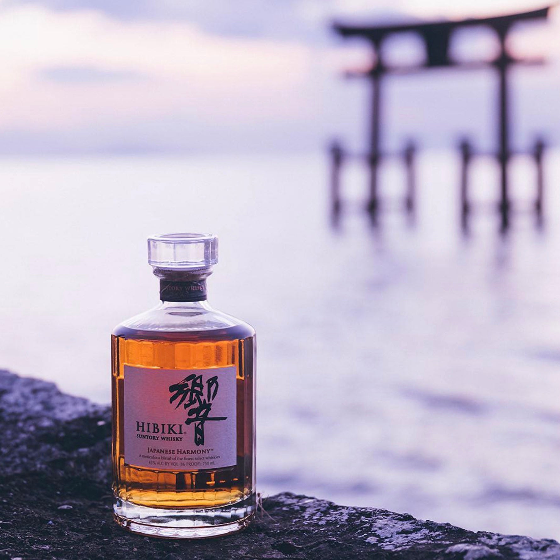 Hibiki Harmony Japanese Whisky bottle with amber liquid against a serene water backdrop, highlighting its elegance and craftsmanship.