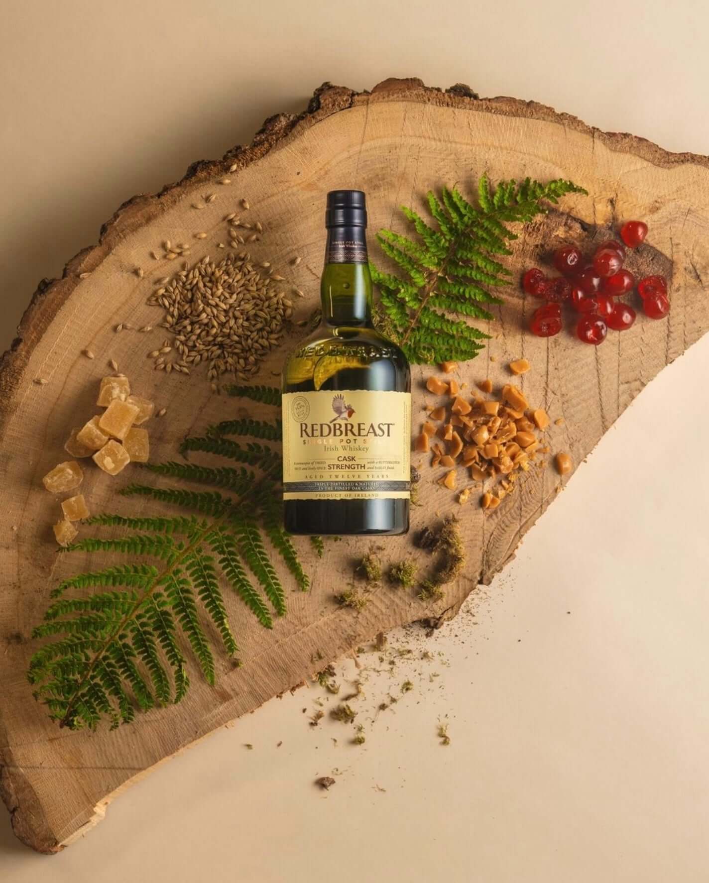 Redbreast Cask Strength 12 Year Irish Whiskey on wood slice with herbs, spices, and fruit accents.