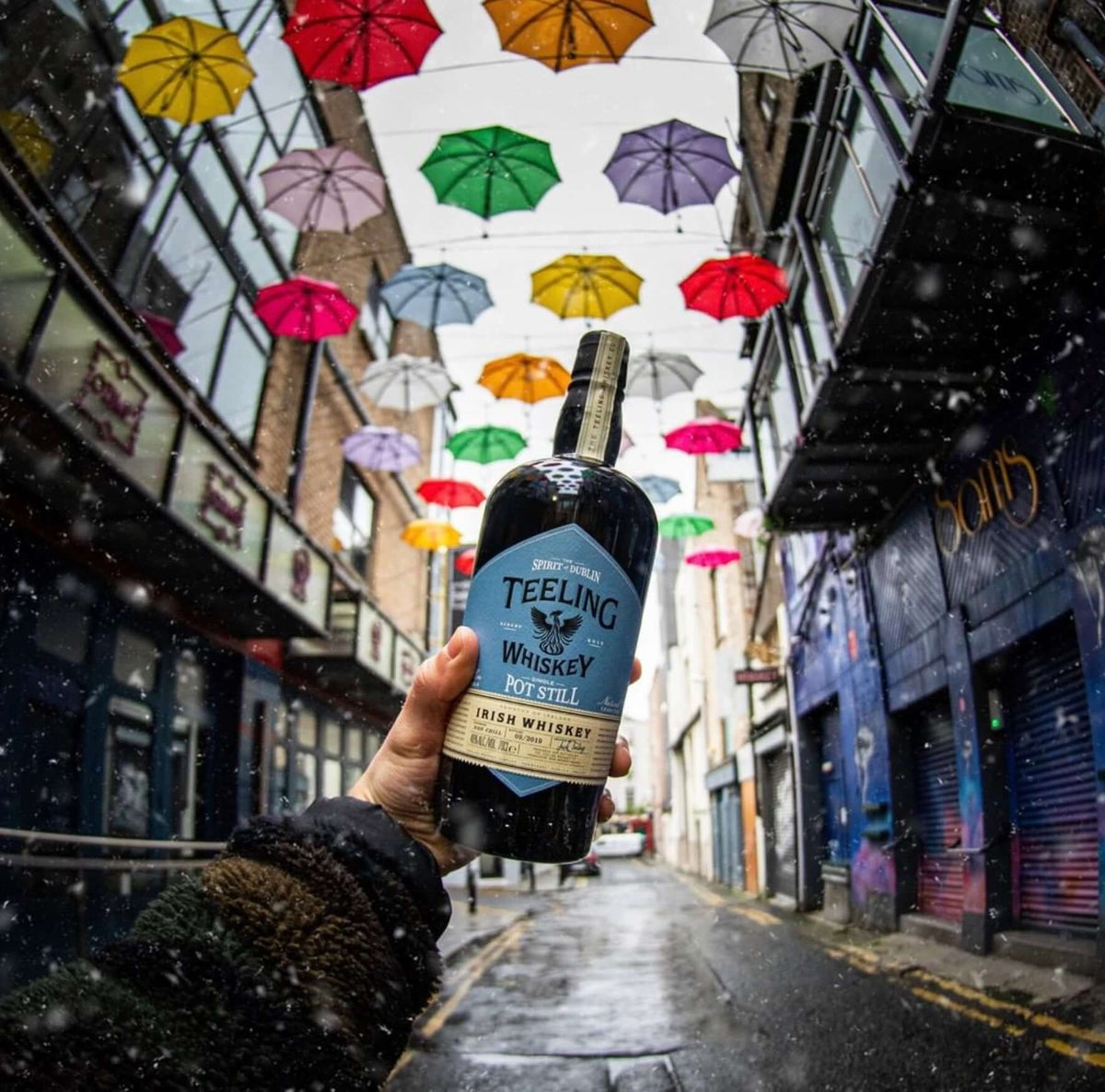 Teeling Single Pot Still Irish Whiskey bottle held in a vibrant Dublin alley with colorful umbrellas.