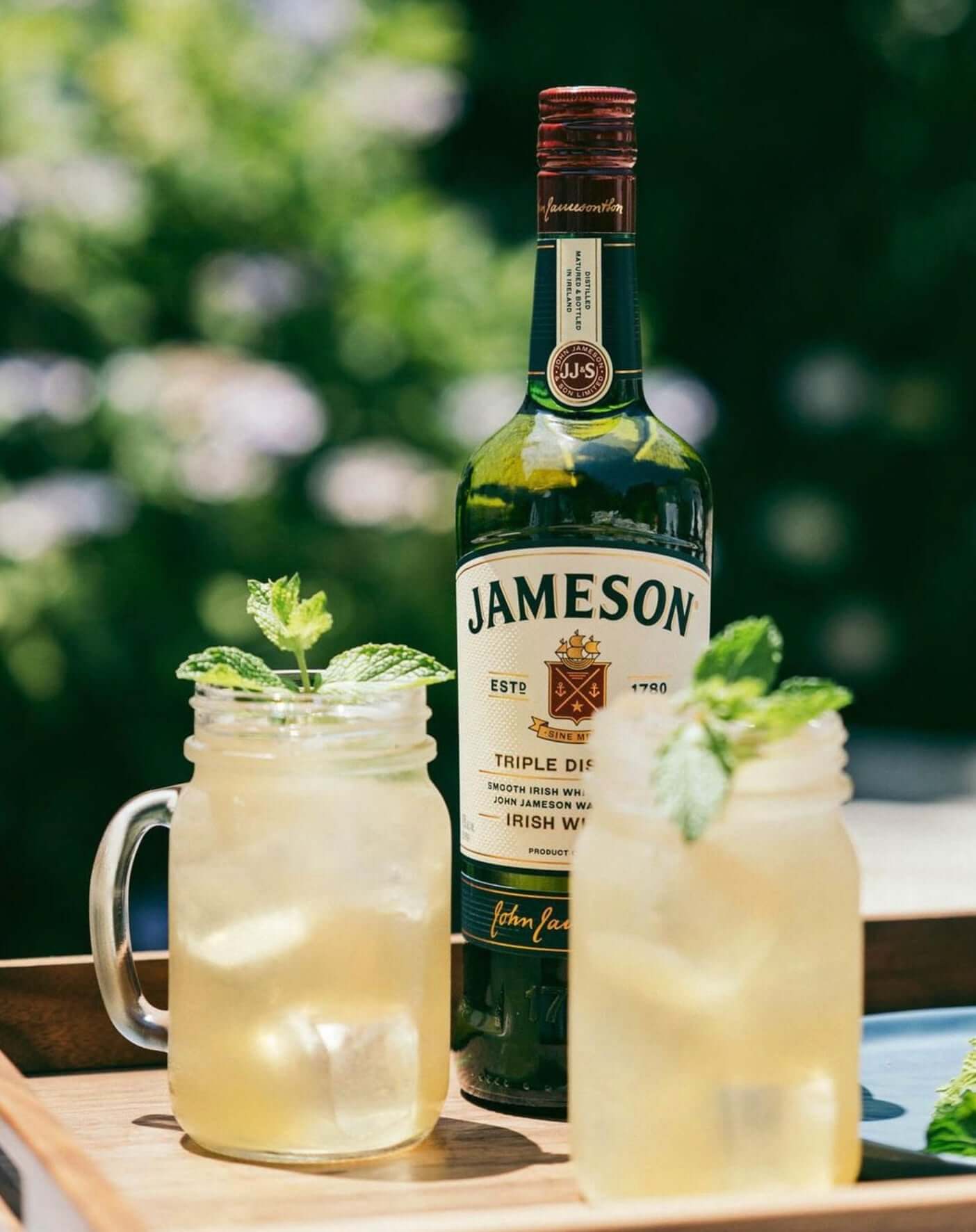 Jameson Irish Whiskey bottle with two refreshing cocktails garnished with mint in mason jars.