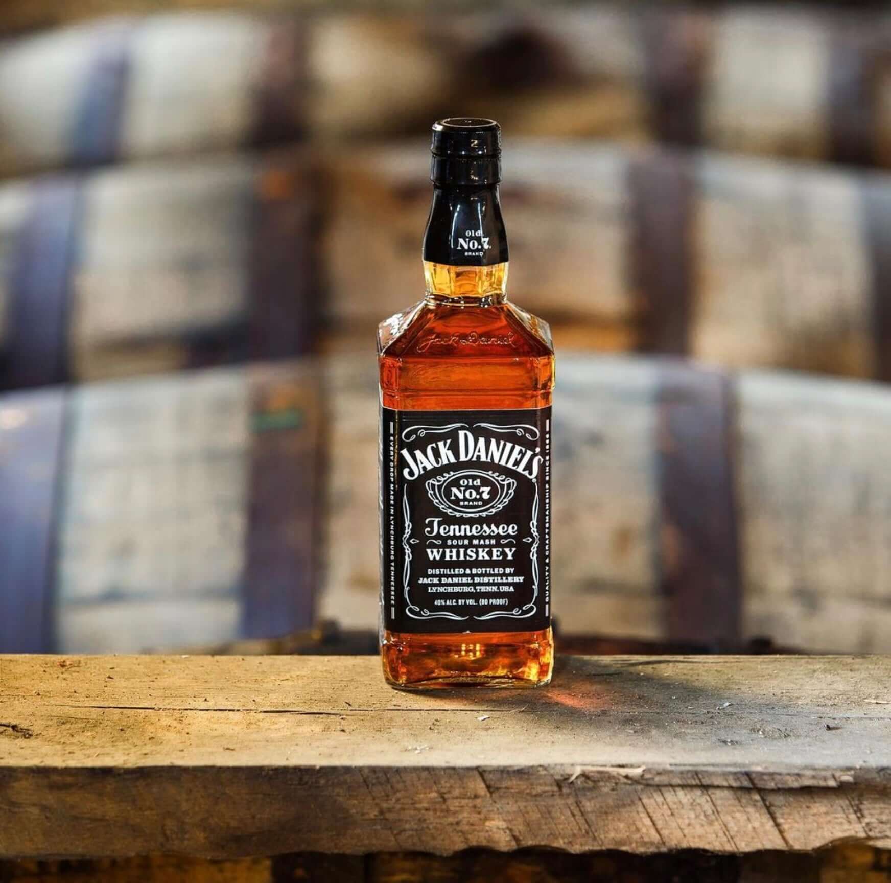 Jack Daniel's Tennessee Whiskey bottle on a rustic wooden surface, with barrels in the background.