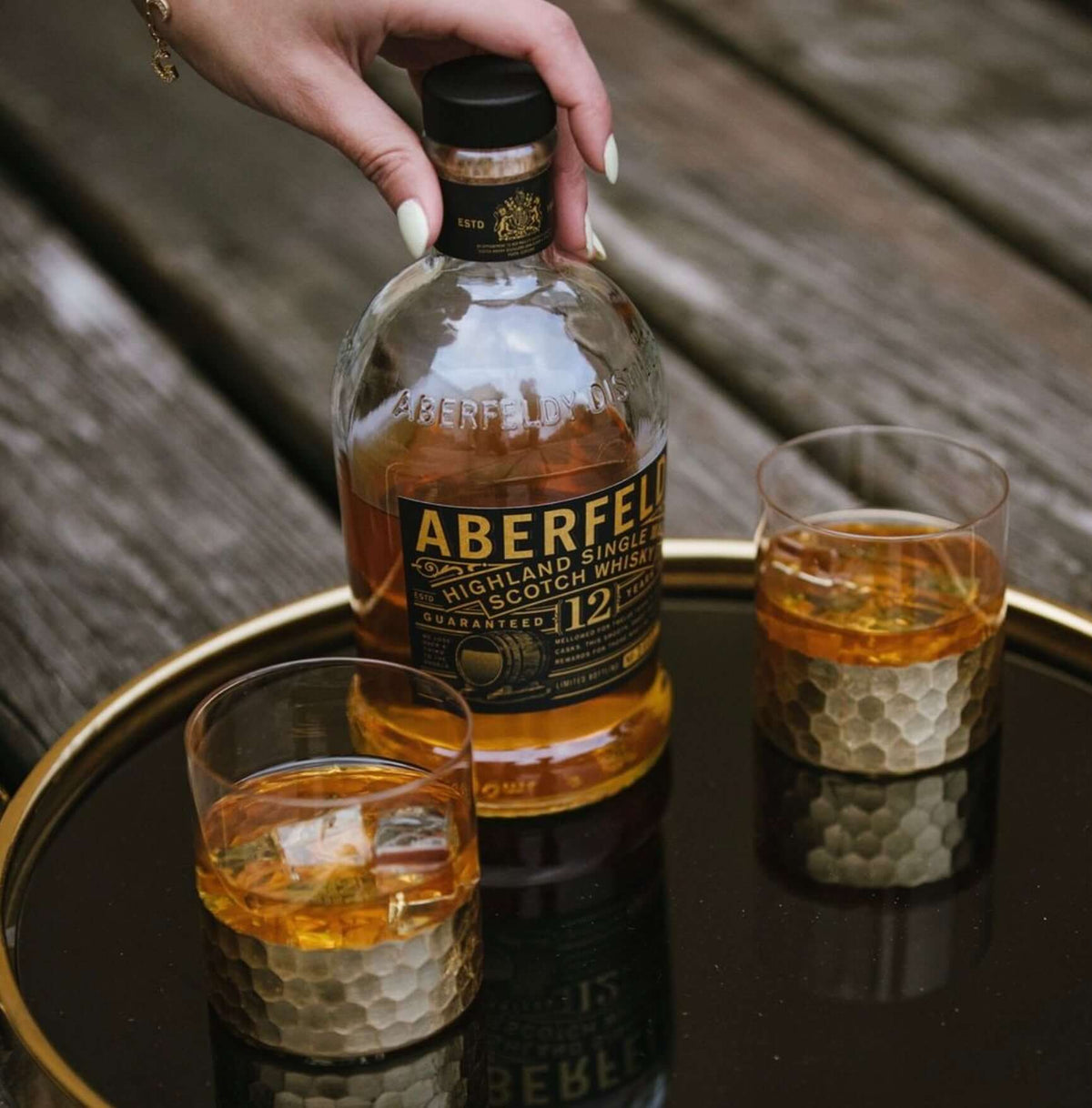 Aberfeldy 12 Year Scotch whisky bottle with two glasses on a low table, showcasing the golden spirit.