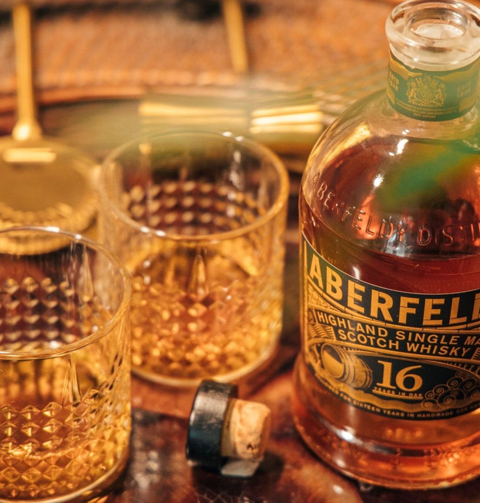 Aberfeldy 16 Year Single Malt Scotch Whisky bottle with two glasses, showcasing a rich amber spirit against a warm backdrop.