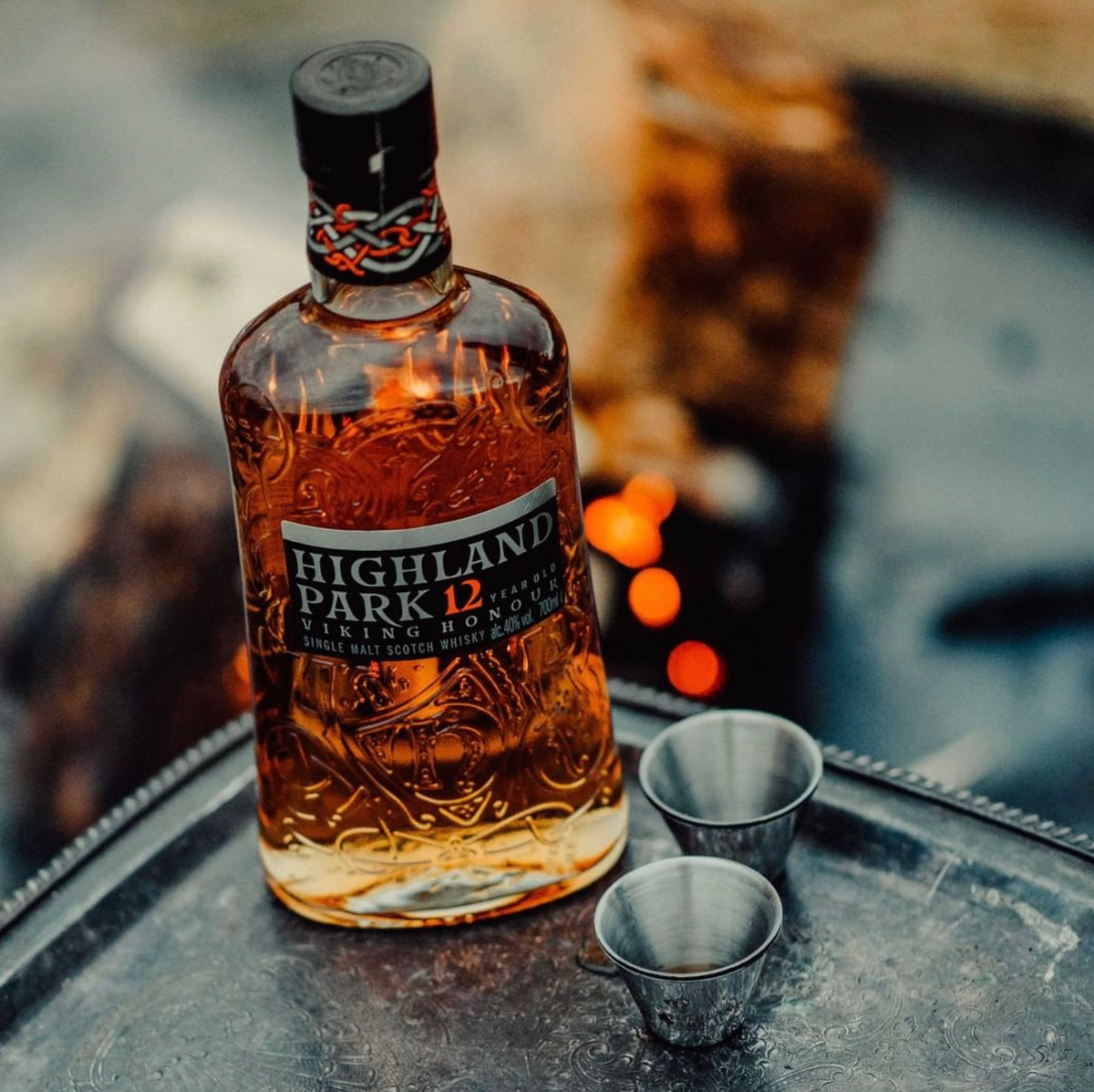Highland Park 12 Year single malt whisky bottle with two metal tasting cups on a rustic tray.