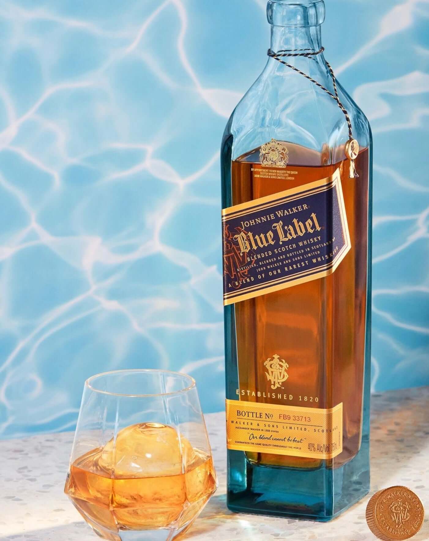 Bottle of Johnnie Walker Blue Label whisky beside a glass with ice, set against a blue background.