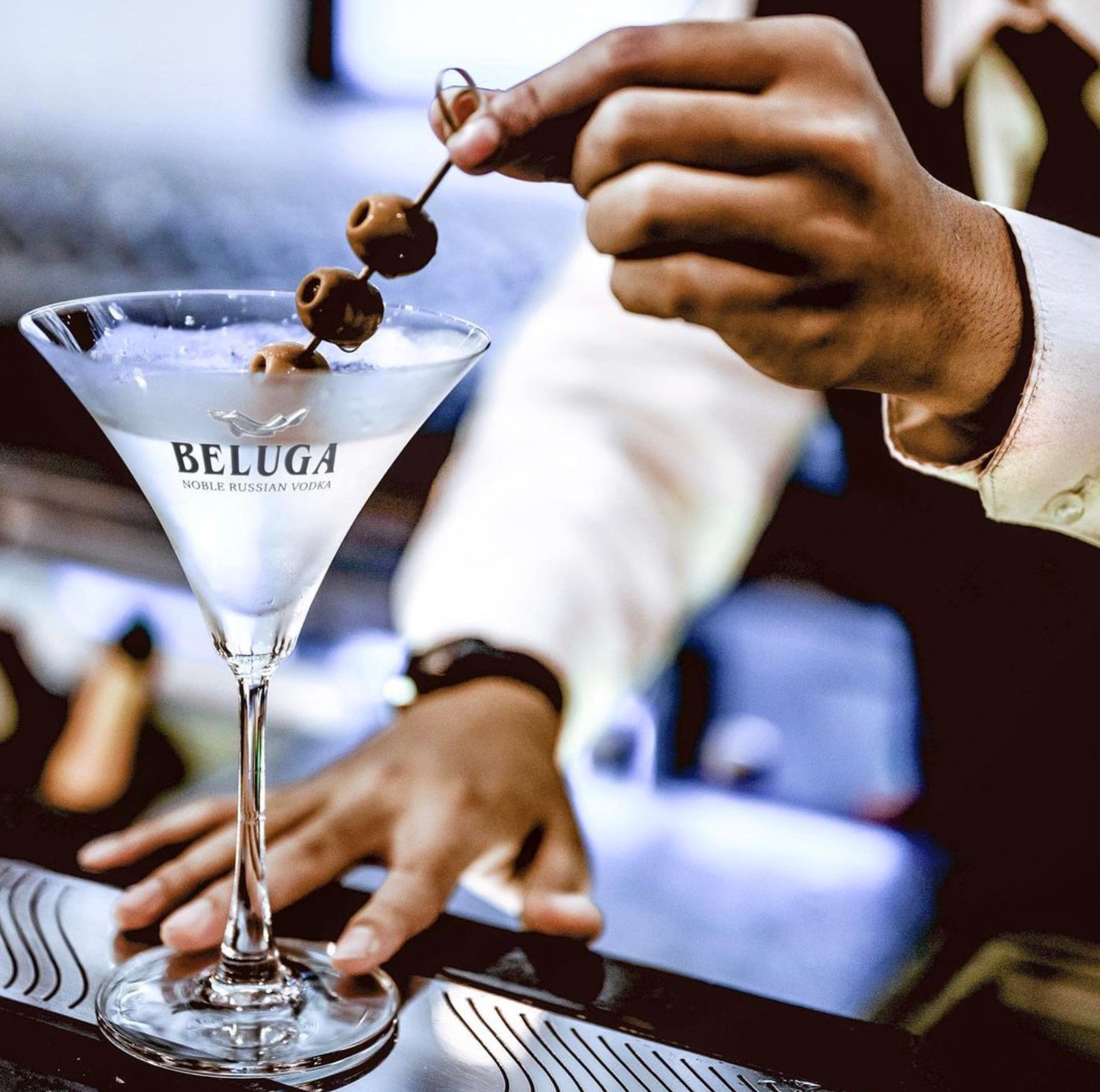 Hand holding a martini glass with Beluga vodka and olives, showcasing a refined cocktail experience.