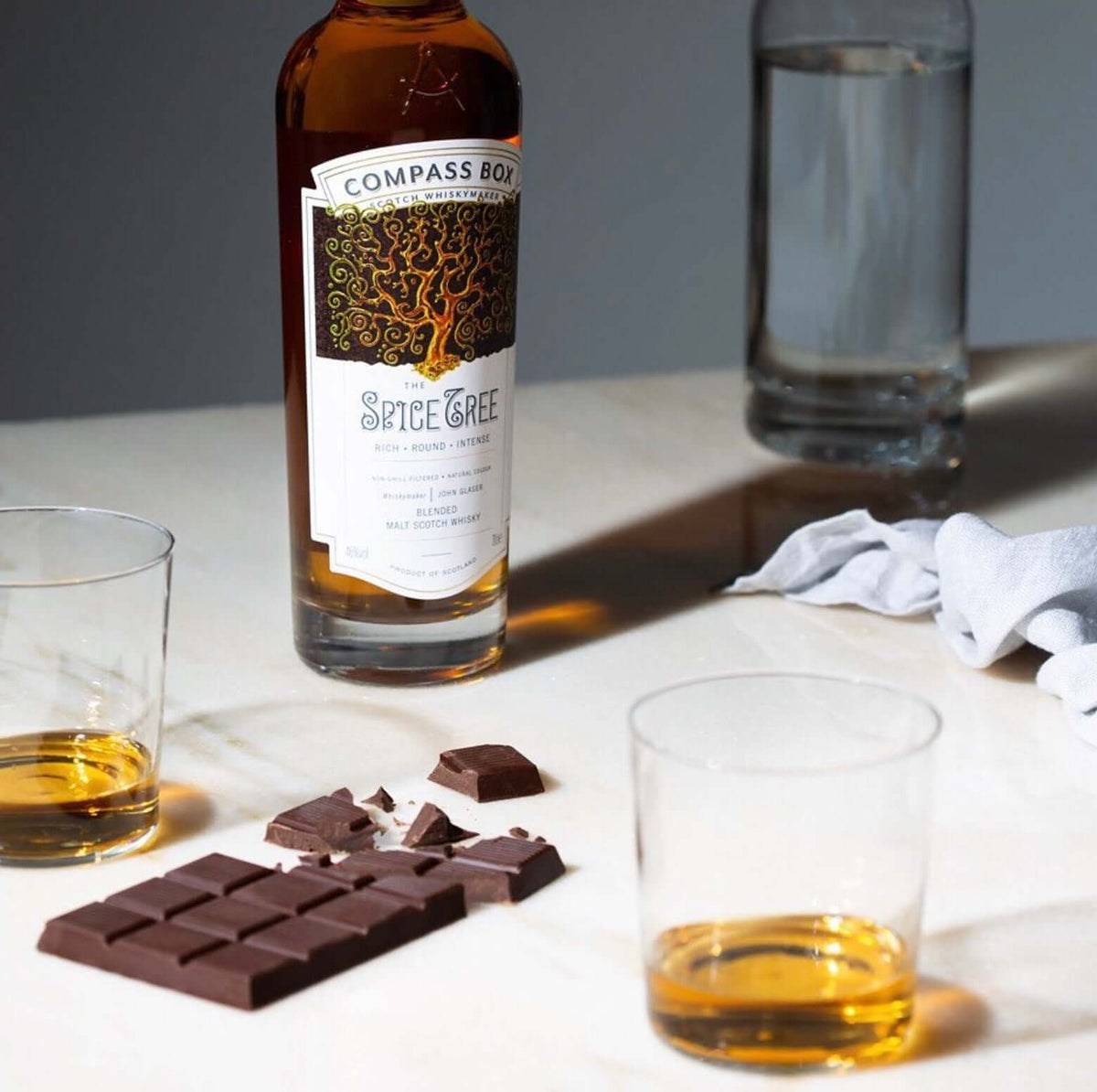 Compass Box Spice Tree Scotch bottle beside glasses and chocolate for a luxurious tasting experience.