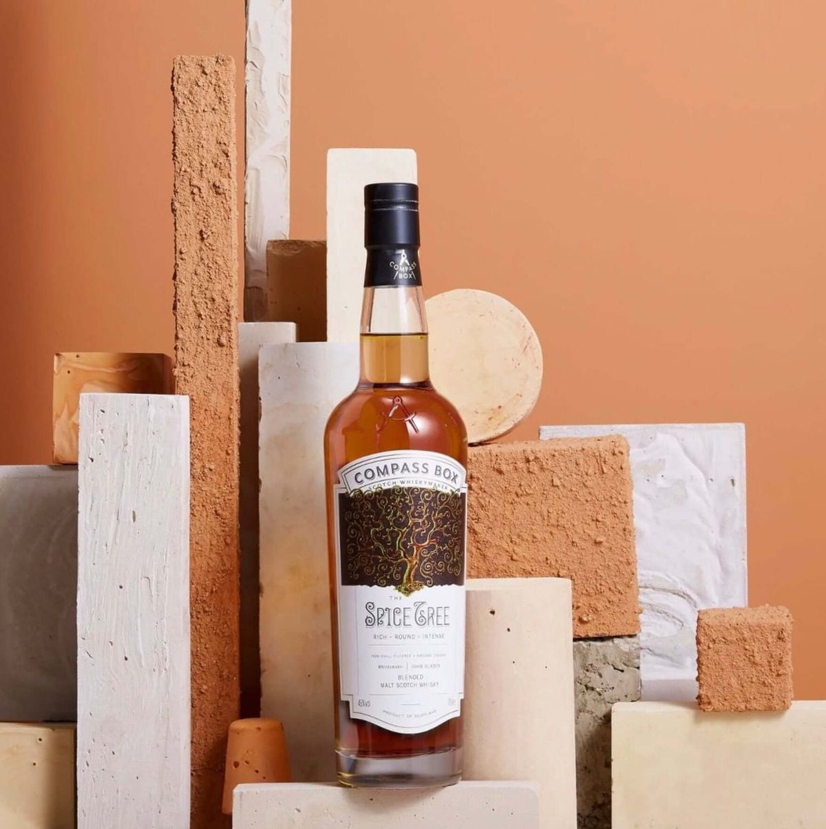Compass Box Spice Tree Scotch bottle displayed among unique textures and colors, showcasing its elegant design.