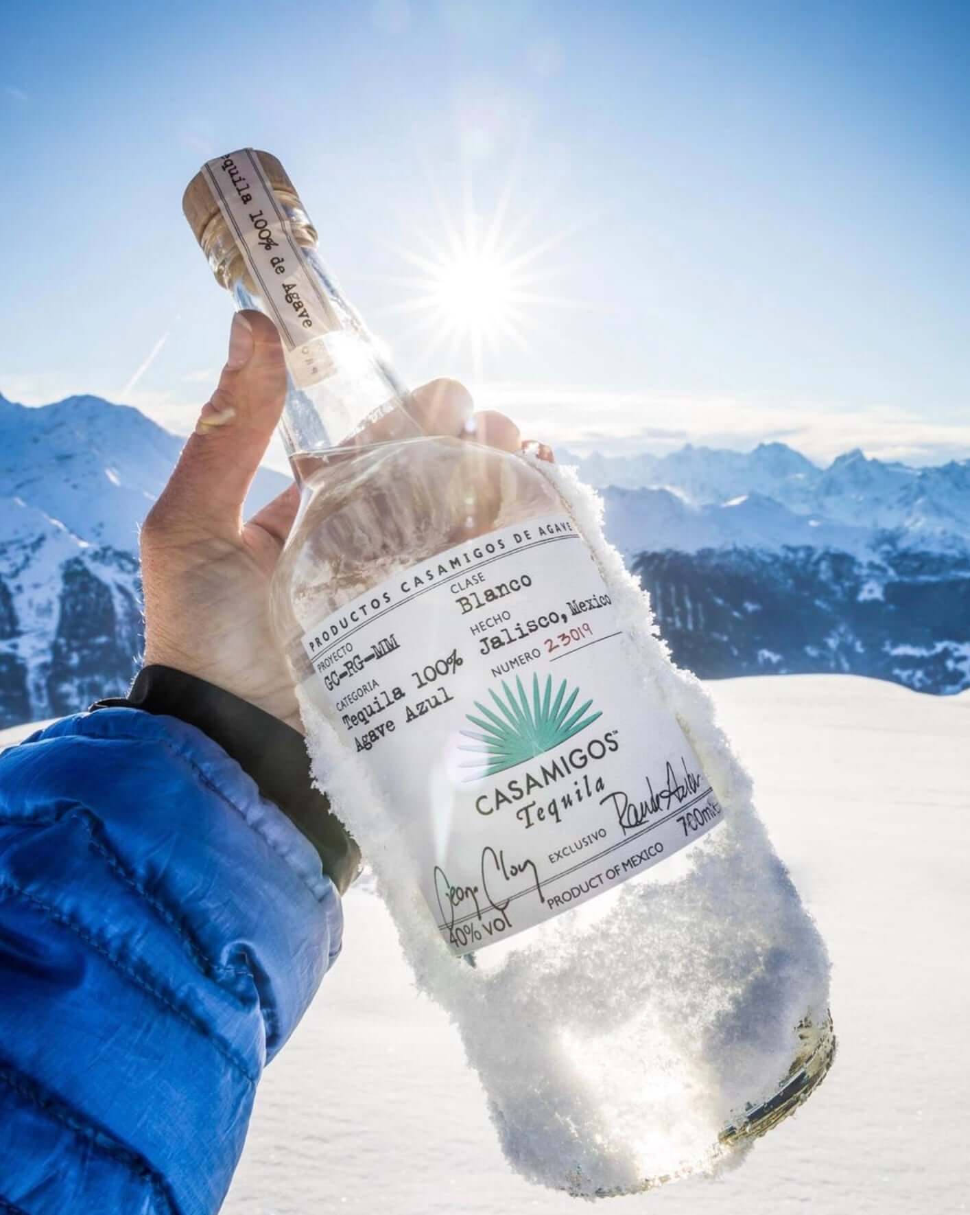 Hand holding Casamigos Blanco Tequila bottle in snowy mountain landscape, showcasing its premium quality and craftsmanship.