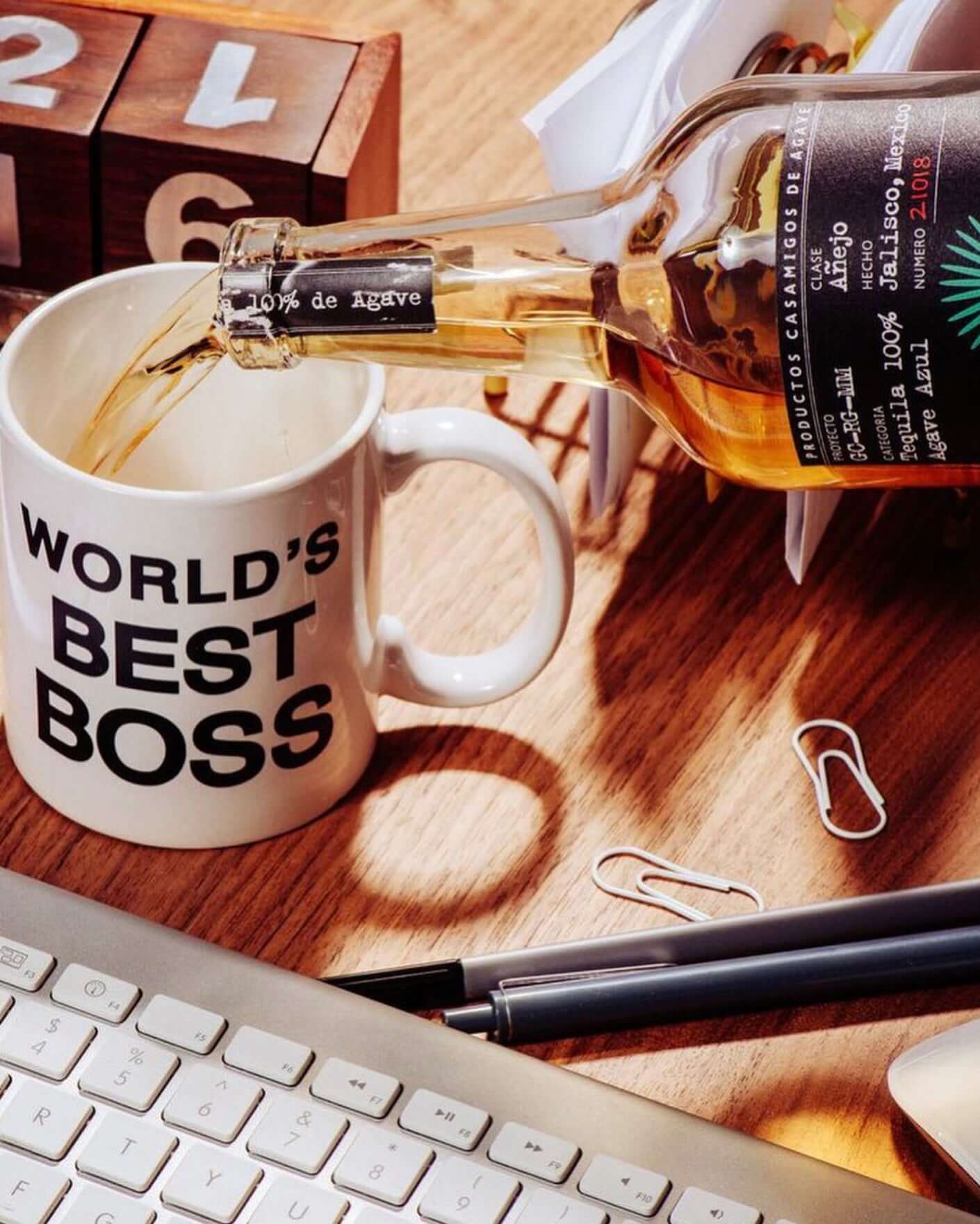 Casamigos Añejo Tequila being poured into a 'World's Best Boss' mug, set on a desk with office supplies.