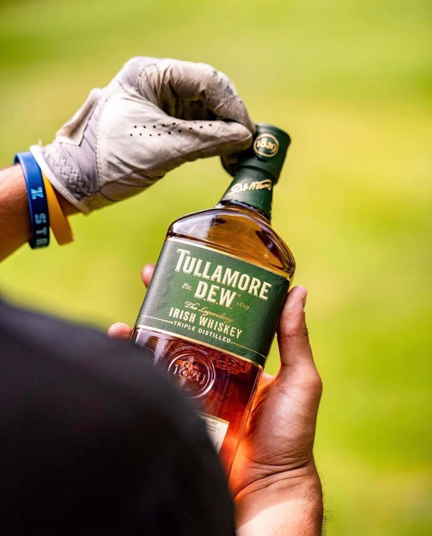 Person holding a bottle of Tullamore Dew Original Irish Whiskey outdoors, showcasing its rich amber color.