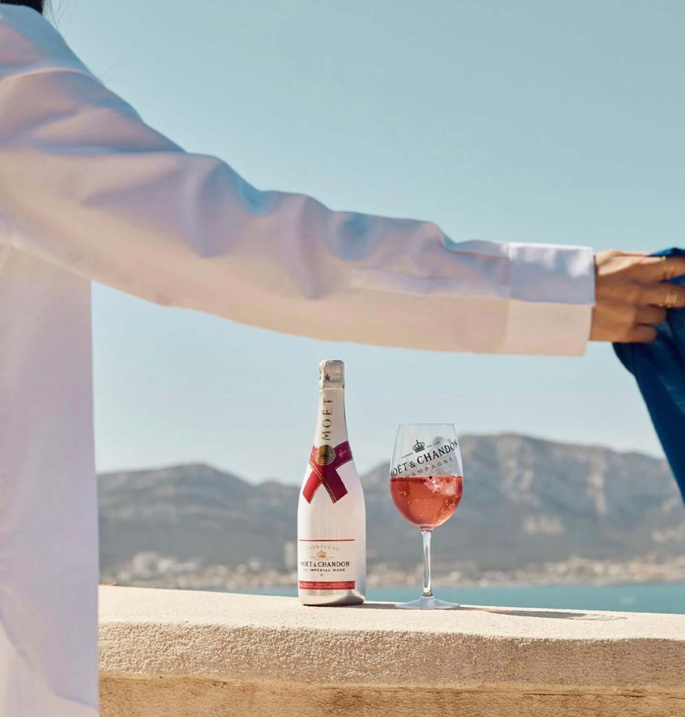 Bottle of Moët & Chandon Ice Impérial Rosé with a glass, set against a scenic coastal backdrop.