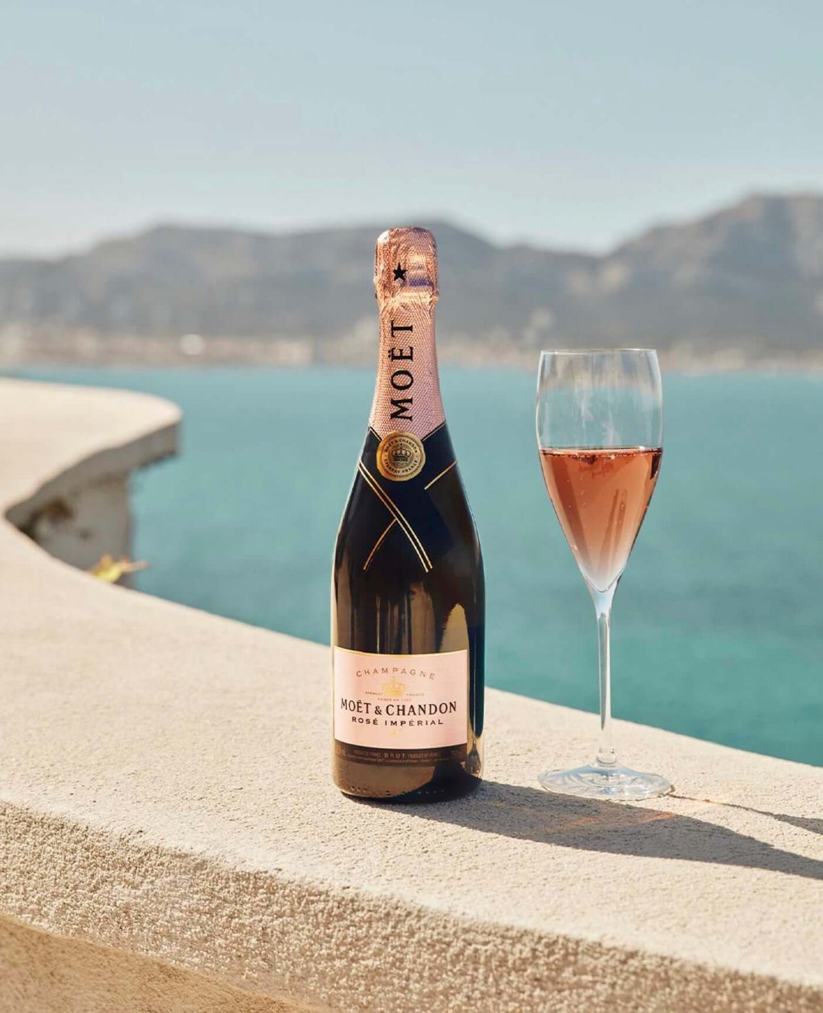 Bottle of Moët & Chandon Rosé Impérial with a glass, overlooking a serene beach view.