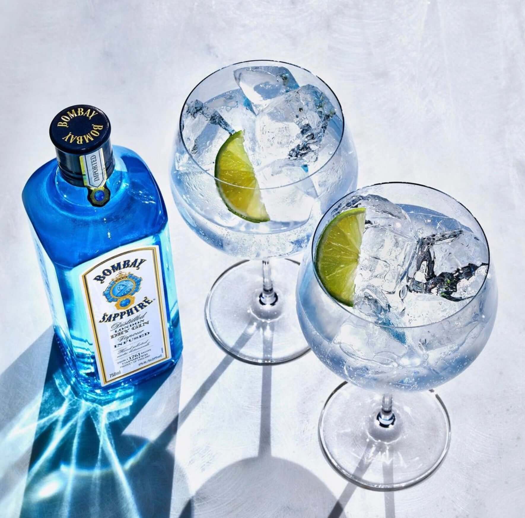 Bombay Sapphire gin bottle with two elegant cocktails garnished with lime and ice.