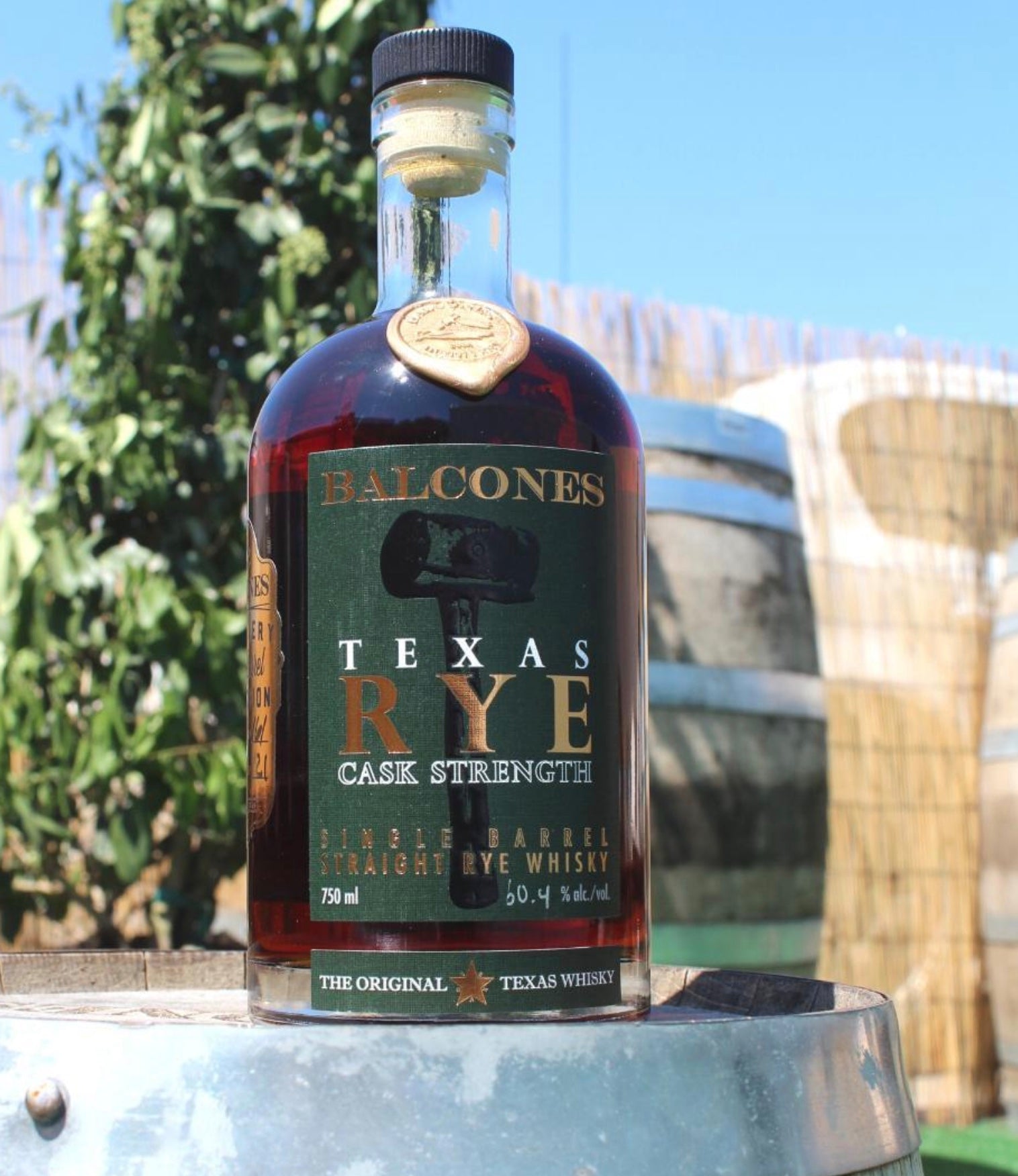 Balcones Texas Rye Cask Strength bottle with charred oak barrels in the background, highlighting premium rye whisky.