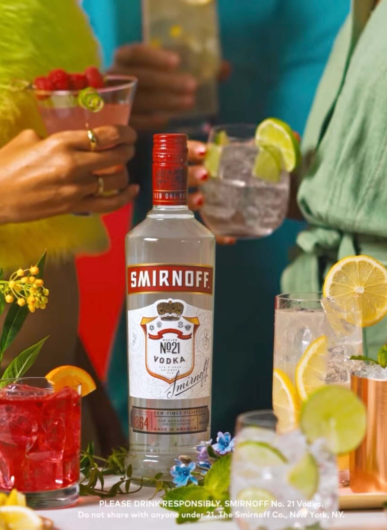 Smirnoff No. 21 vodka bottle displayed at a vibrant cocktail party with mixed drinks and garnishes.