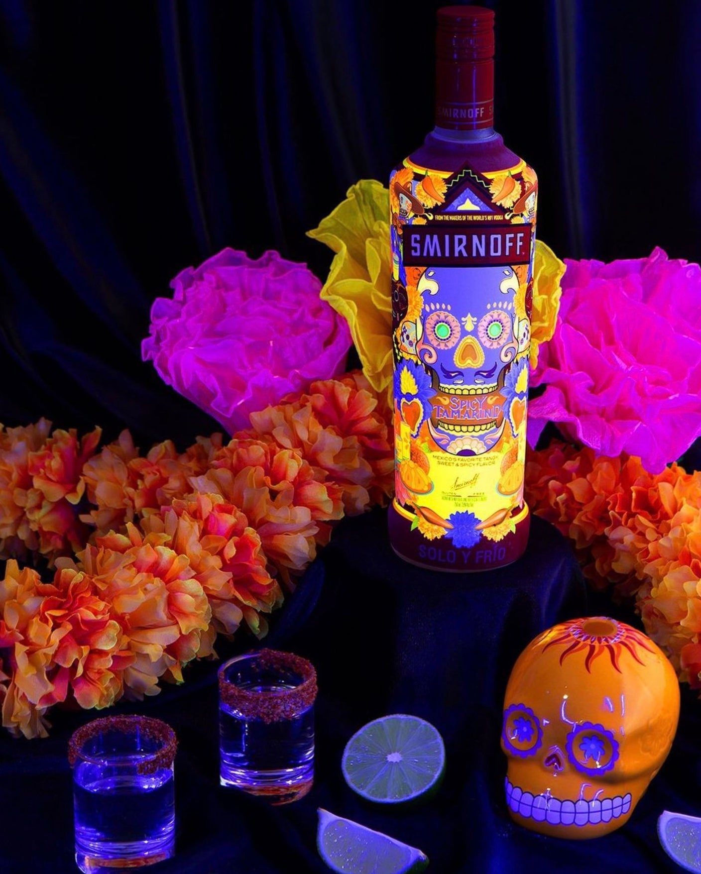 Smirnoff Spicy Tamarind Vodka bottle surrounded by vibrant flowers and shot glasses, evoking a festive atmosphere.