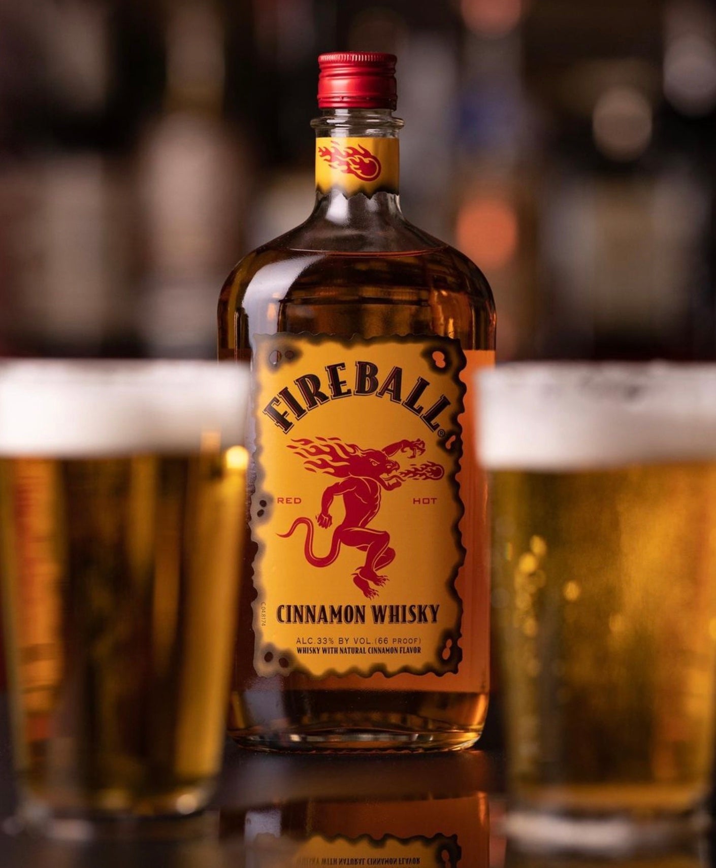 Fireball Cinnamon Whisky 750ml bottle with two glasses of beer, showcasing vibrant label and rich colors.
