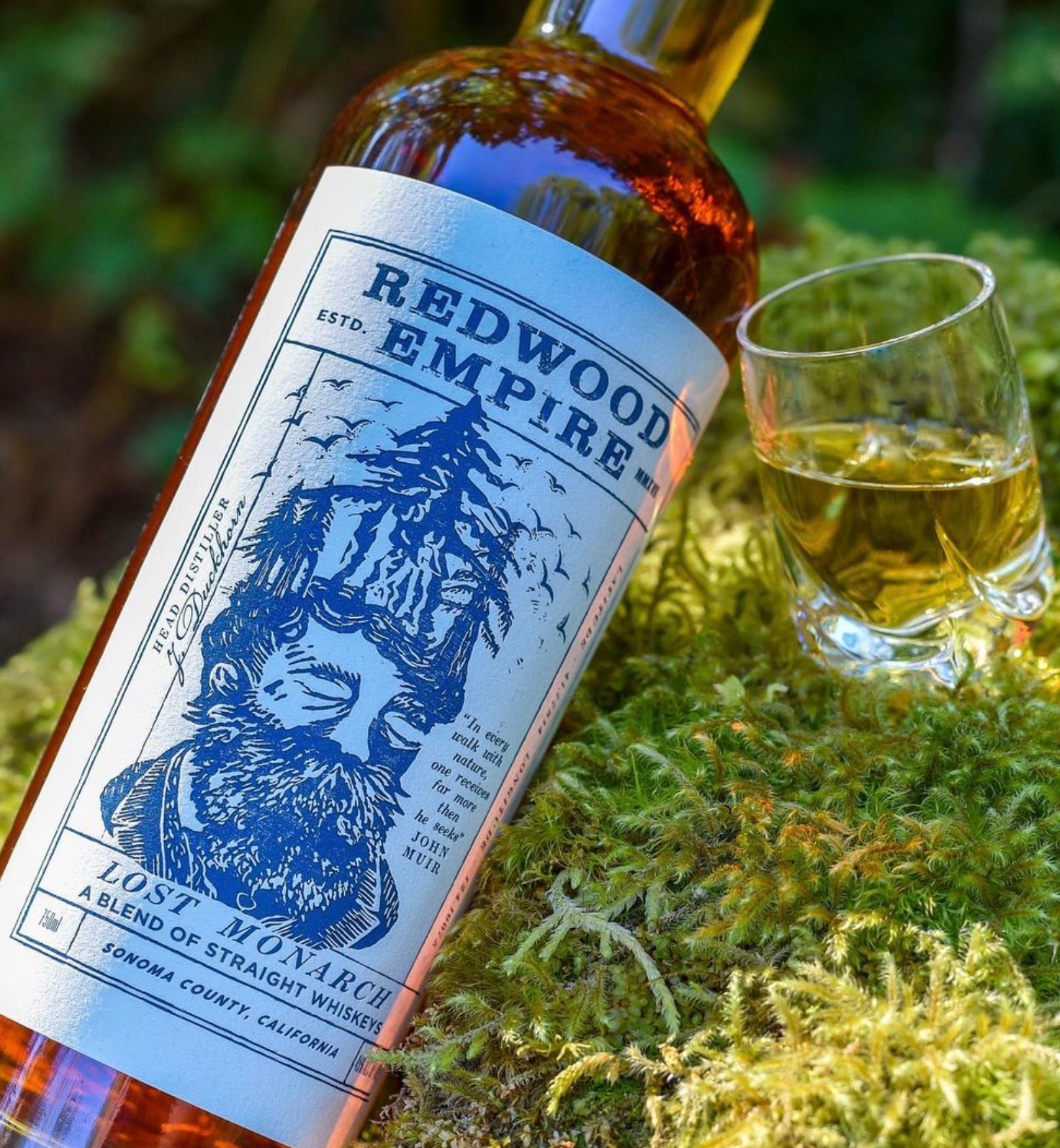 Redwood Empire Lost Monarch whiskey bottle beside a glass, showcasing its dark amber color and rich packaging design.