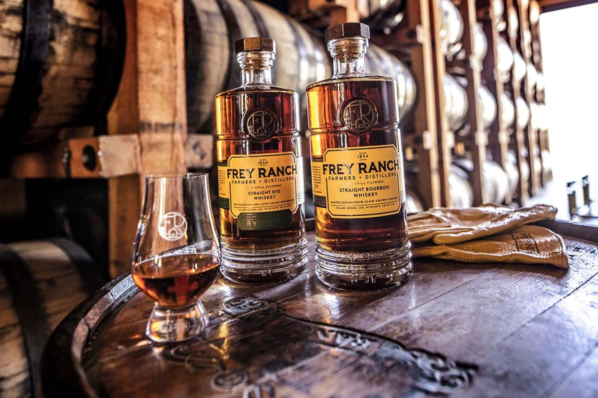Two bottles of Frey Ranch Bottled-in-Bond Straight Rye Whiskey on a wooden barrel, with a tasting glass beside them.
