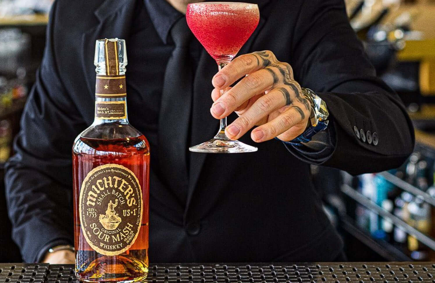 Michter's Sour Mash Whiskey bottle on bar with bartender holding a cocktail, showcasing whiskey's premium quality.
