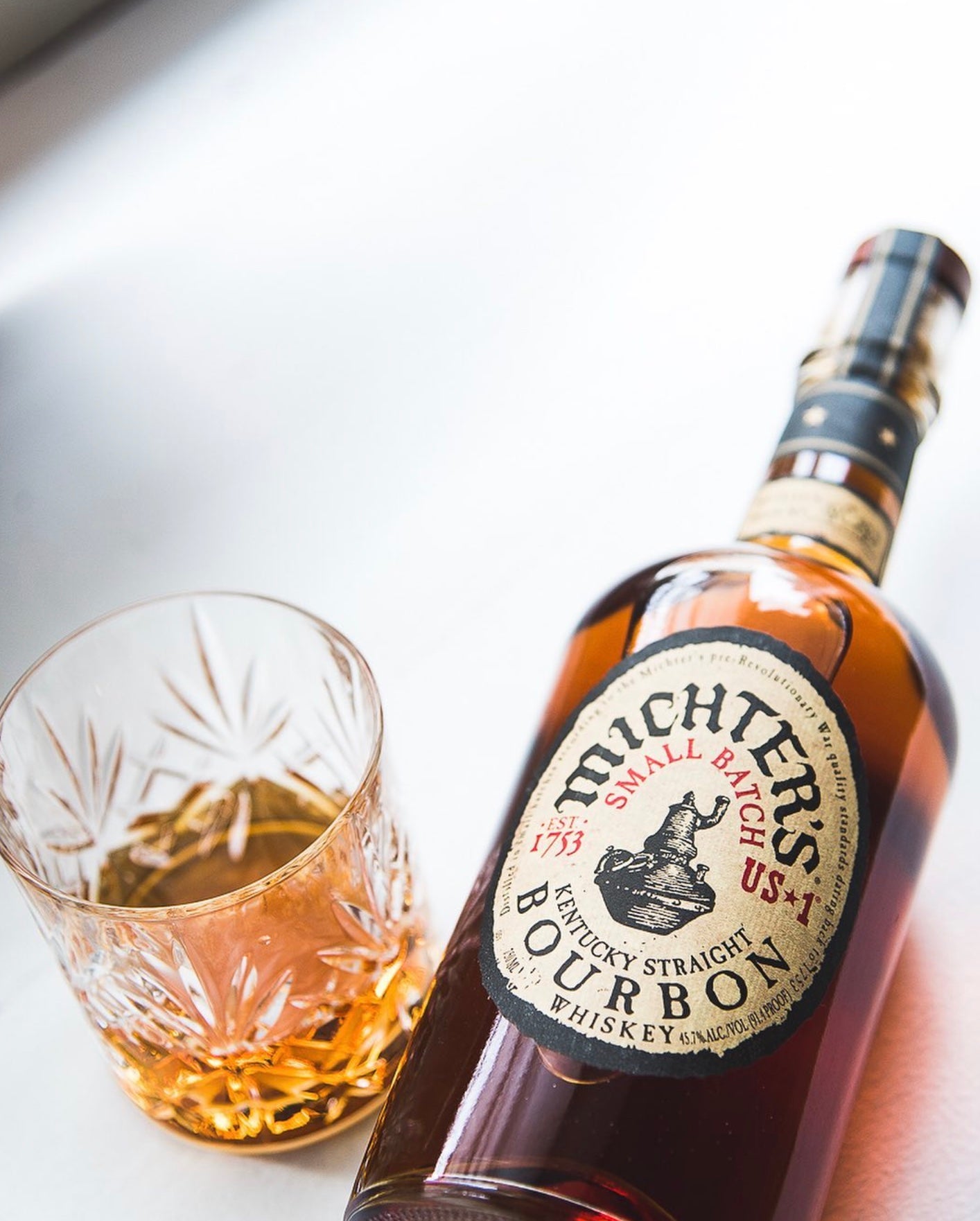 Michter's Small Batch Bourbon bottle beside a glass of bourbon showcasing rich amber color and intricate label details.