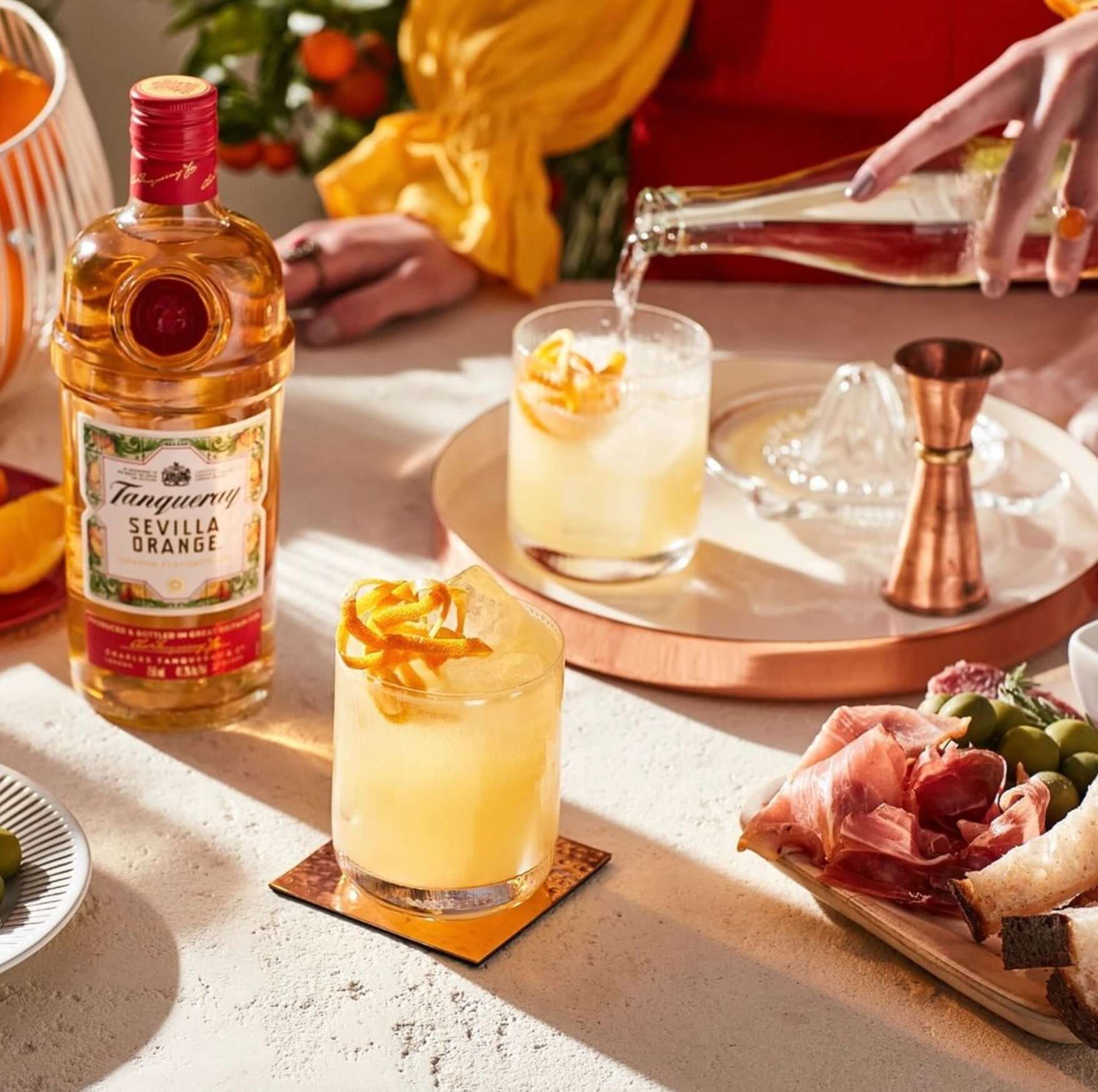 A refreshing cocktail with Tanqueray Sevilla Orange Gin, garnished with orange, served with snacks on a stylish table.