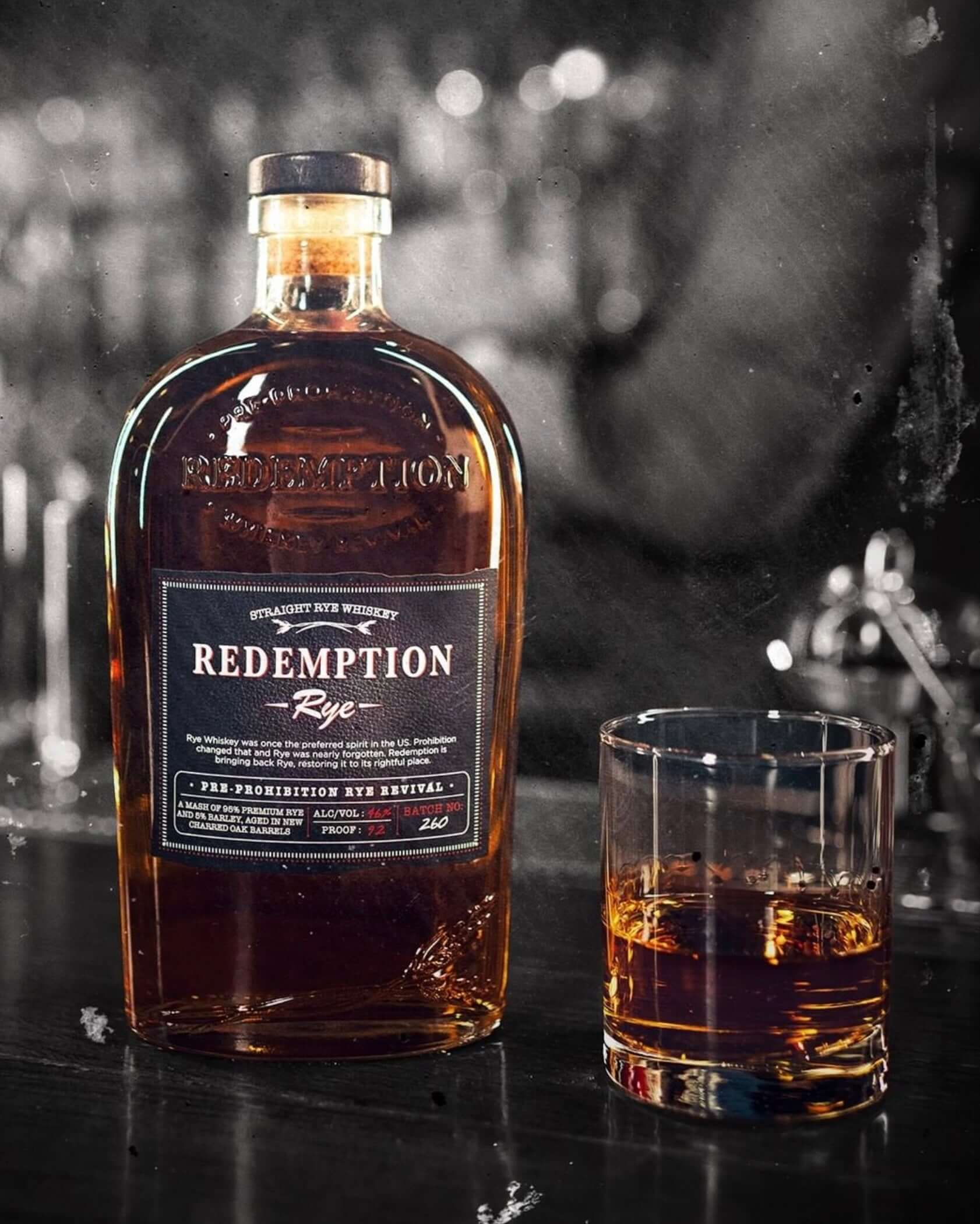 Bottle of Redemption Rye Whiskey with a glass containing whiskey on a bar counter.