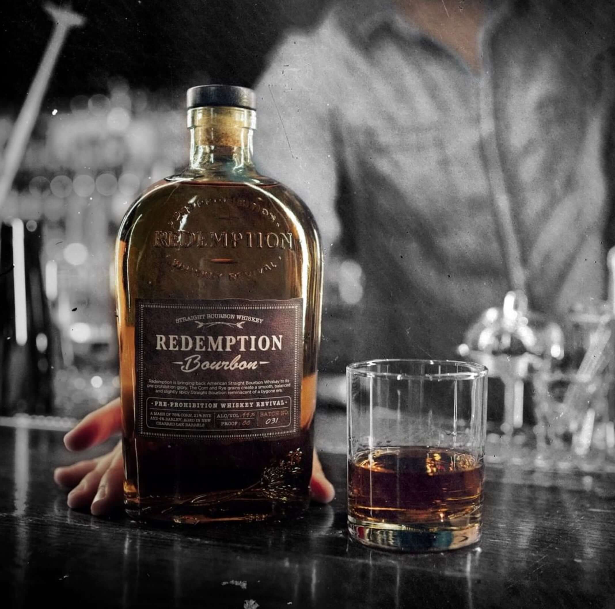 Bottle of Redemption Straight Bourbon with a glass on a bar, showcasing its rich color and smooth character.