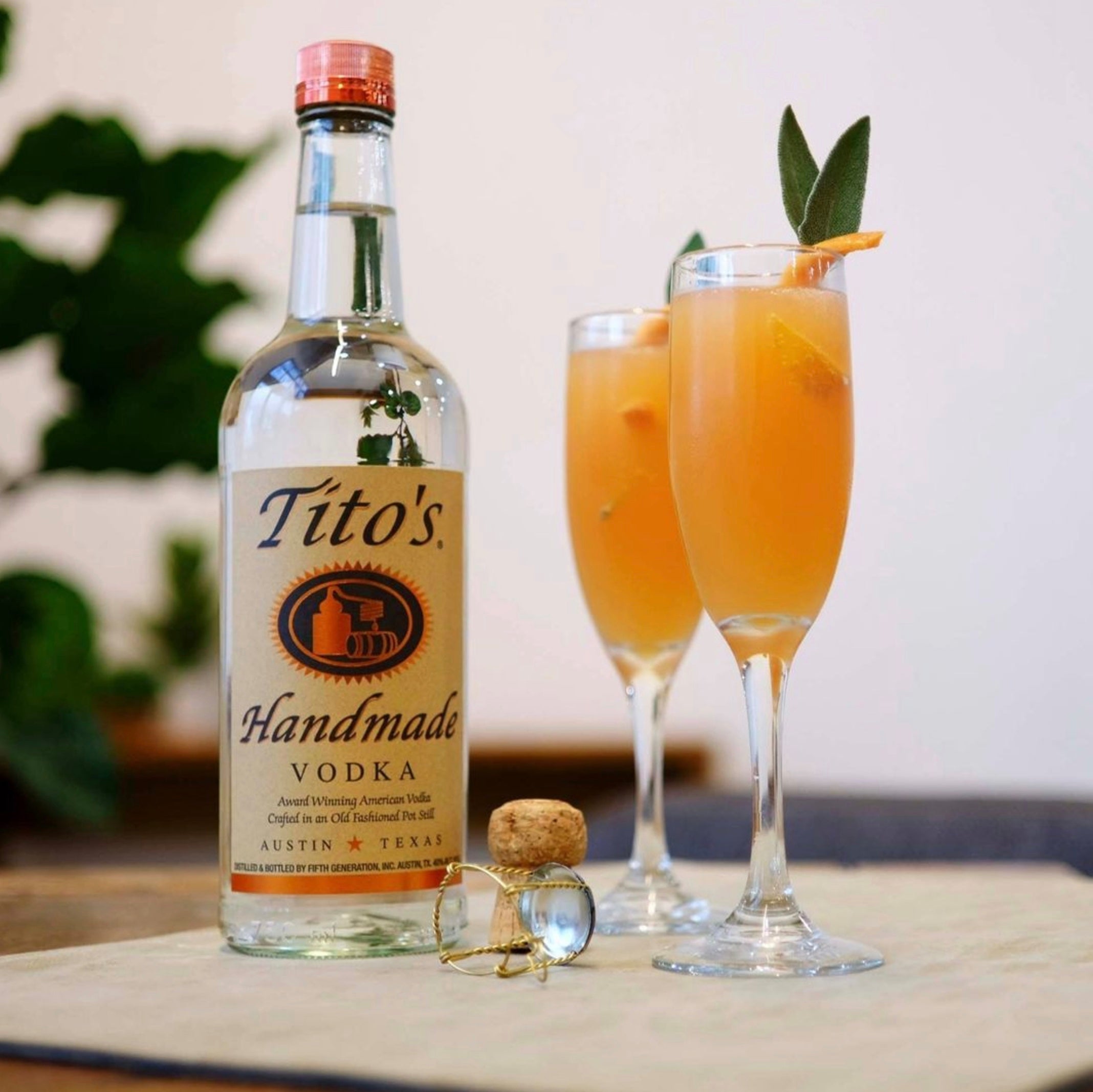 Tito's Handmade Vodka bottle with two stylish cocktails garnished with orange and mint.