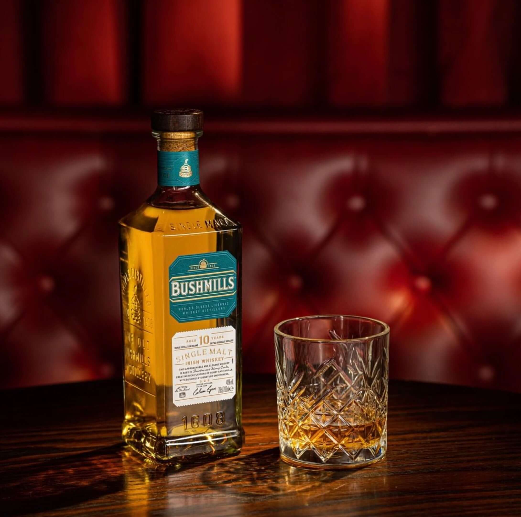 Bushmills 10 Year Single Malt whiskey bottle next to a whiskey glass on a wooden table, elegantly displayed.