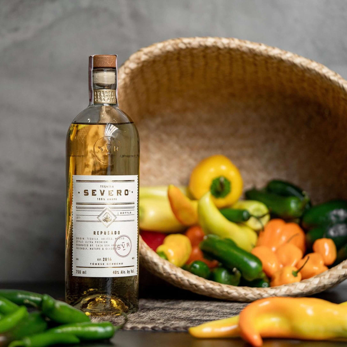 Severo Reposado Tequila bottle with colorful peppers in woven basket, showcasing artisanal craftsmanship and vibrant flavors.