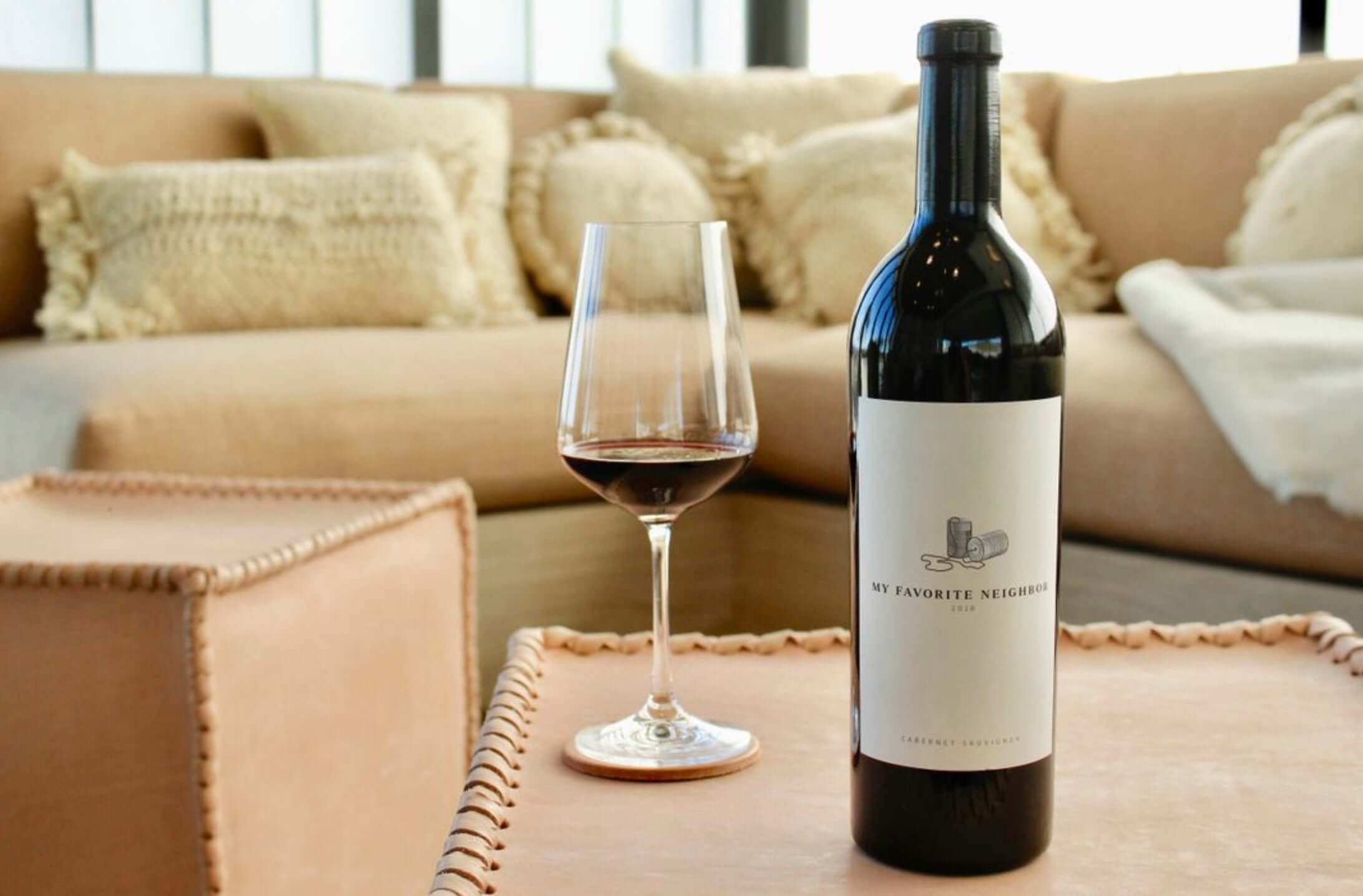 My Favorite Neighbor Cabernet Sauvignon bottle with glass on a stylish wooden table in a cozy living room.