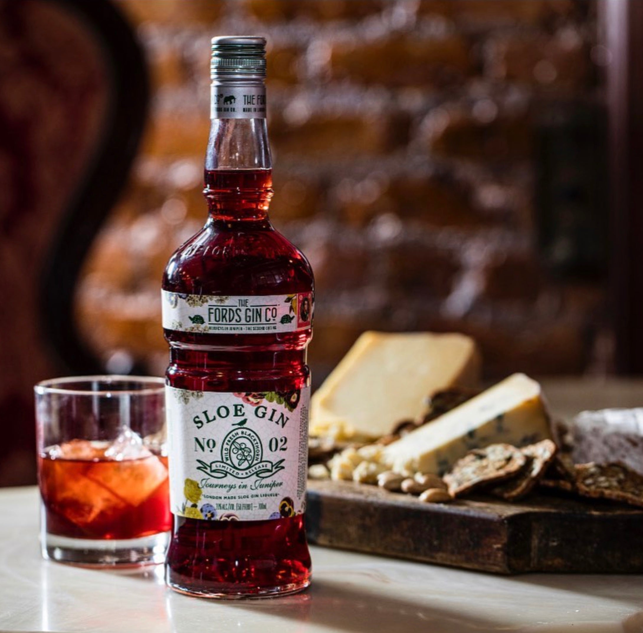 Fords Sloe Gin bottle on table with cocktail glass and cheese platter, perfect for cocktails and gatherings.
