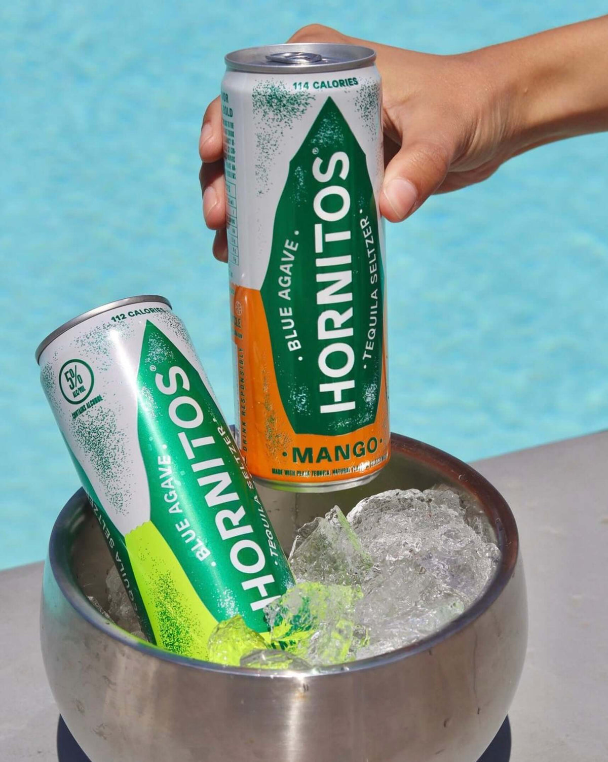 Hornitos Mango Tequila Seltzer cans in ice, perfect for refreshing summer drinks by the pool.