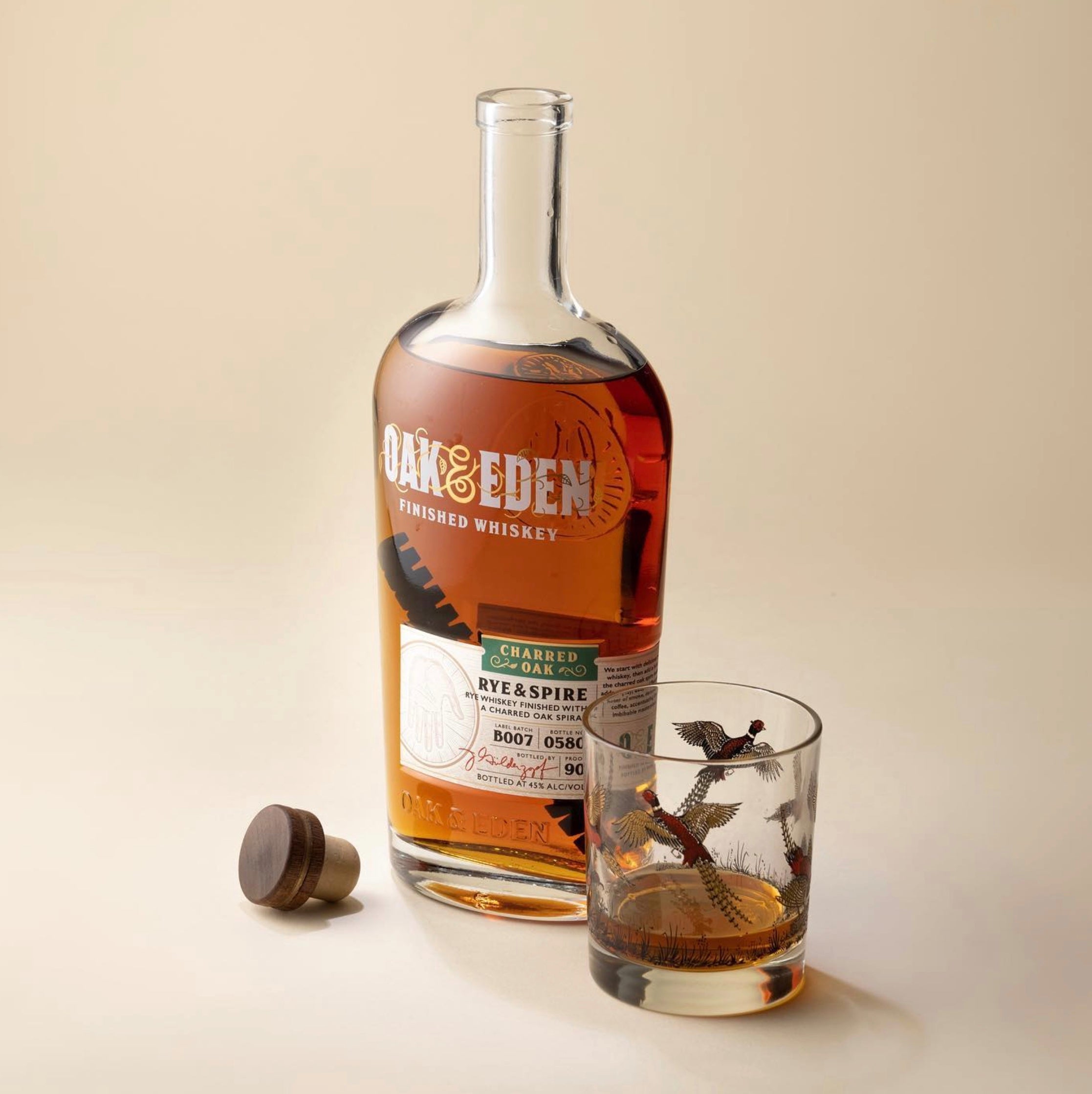 Bottle of Oak & Eden Rye & Spire whiskey next to a glass filled with whiskey, showcasing the rich amber color.