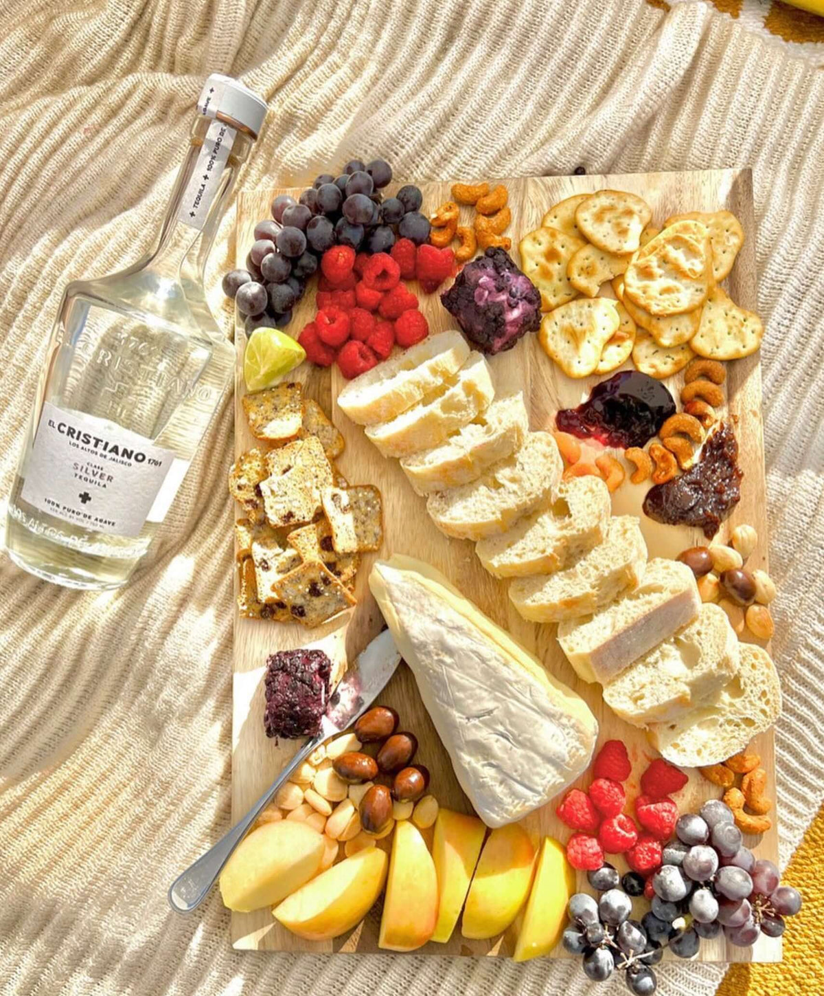 El Cristiano 1761 Silver Tequila paired with a colorful cheese and fruit platter, showcasing vibrant flavors.