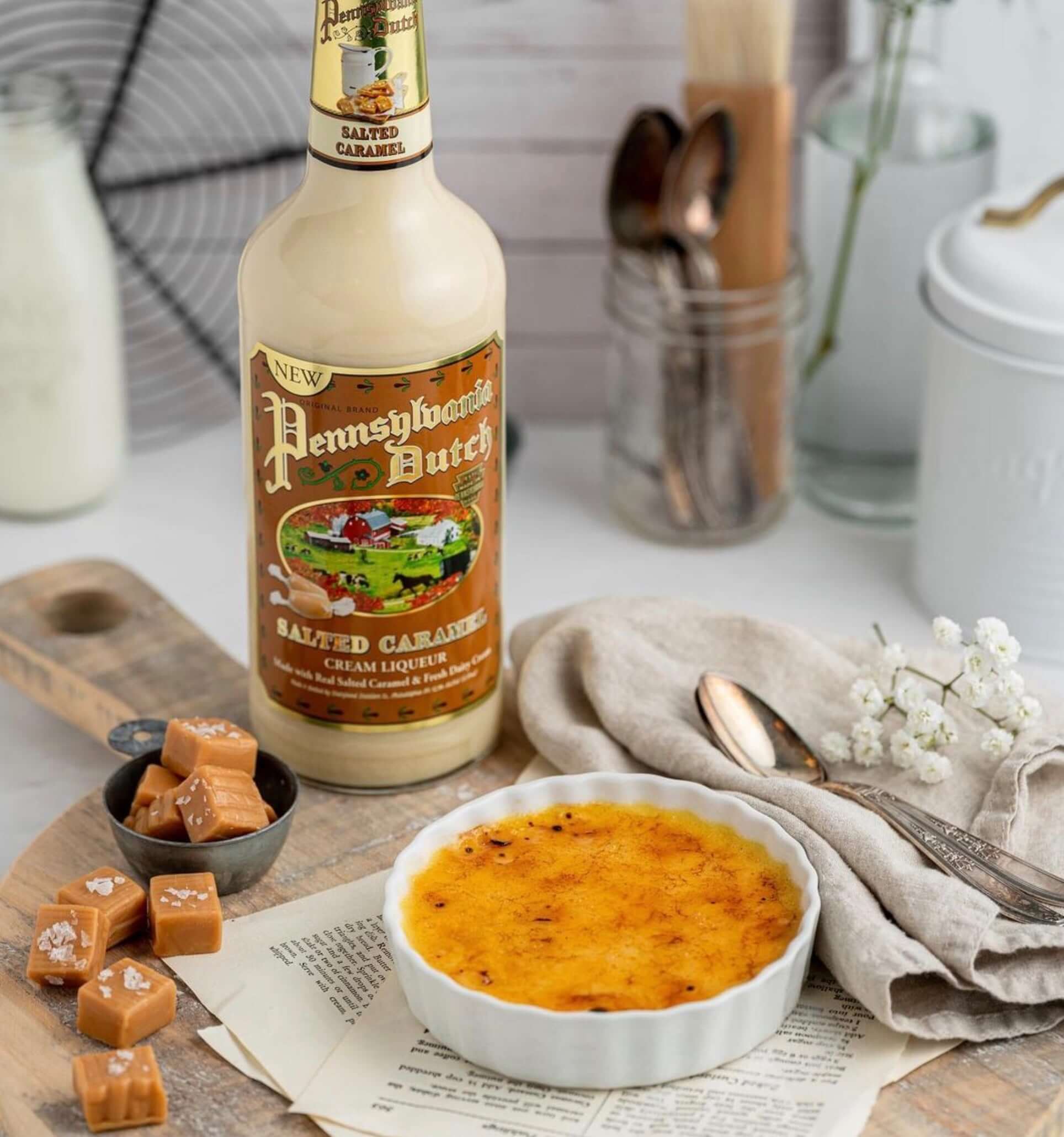 Pennsylvania Dutch Salted Caramel cream liqueur bottle next to caramel candies and a dessert ramekin on a rustic table.