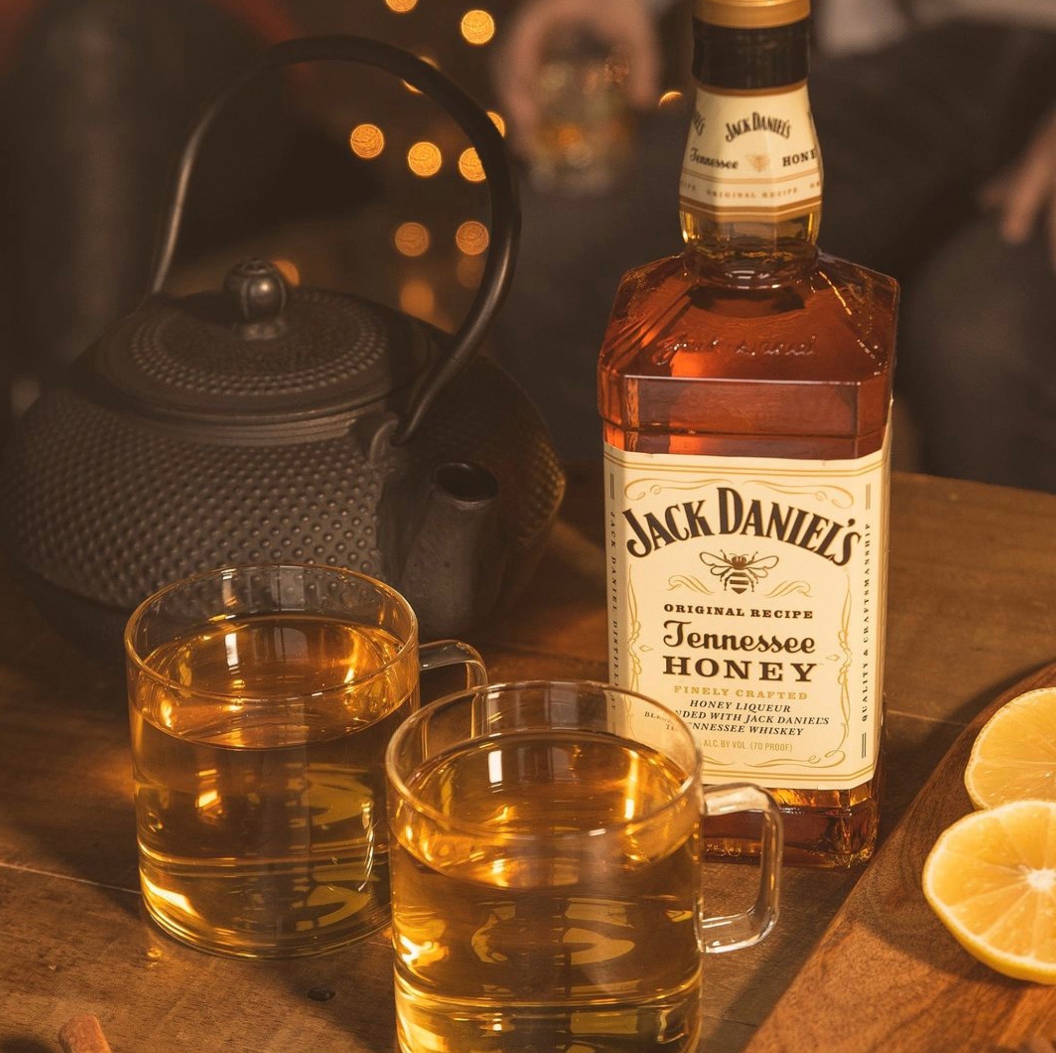 Jack Daniel's Tennessee Honey whiskey bottle with two glasses and a teapot, evoking cozy moments and smooth flavor.