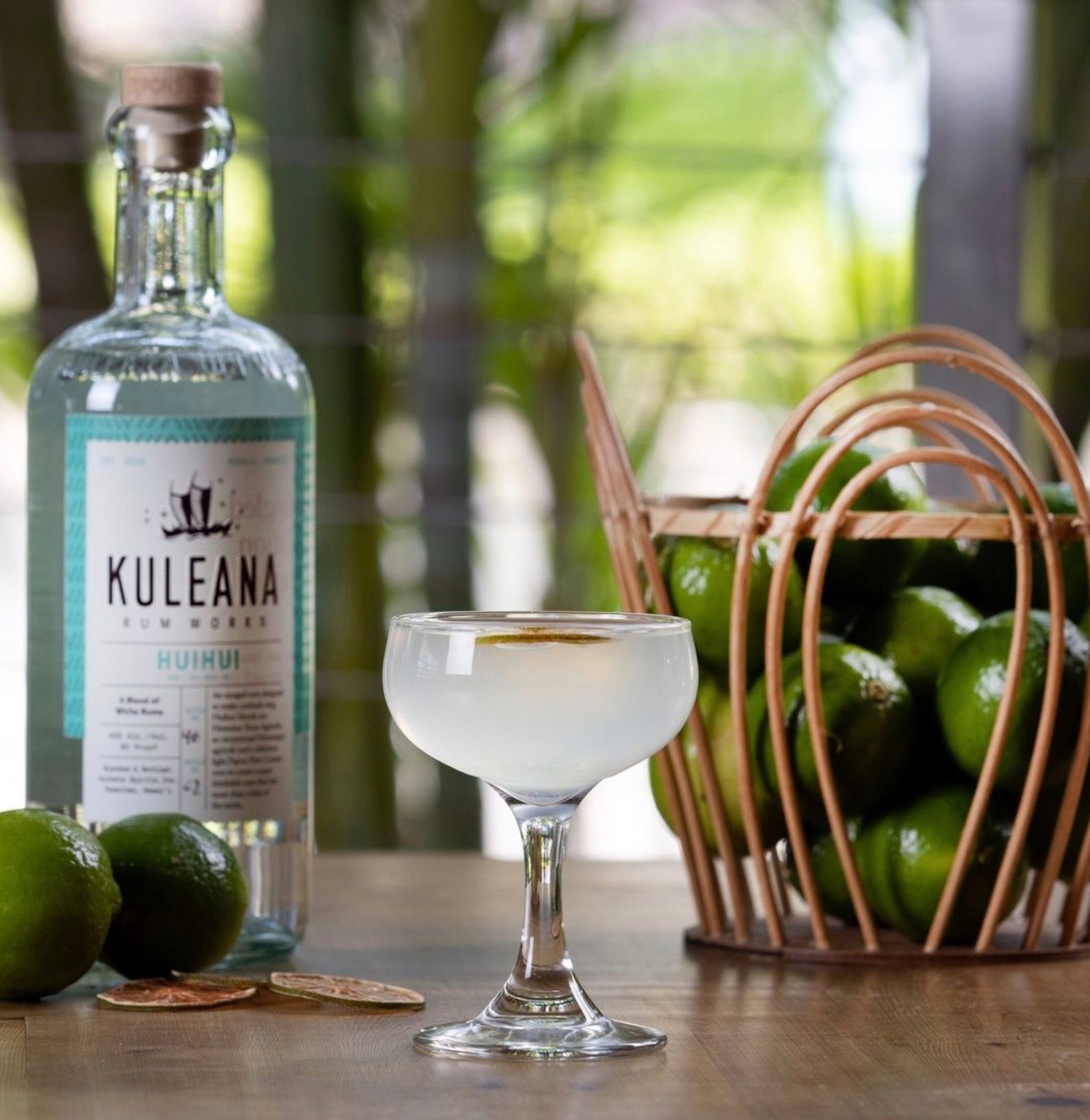 Kuleana Huihui Rum bottle next to a cocktail glass and fresh limes, showcasing an exotic drink experience.
